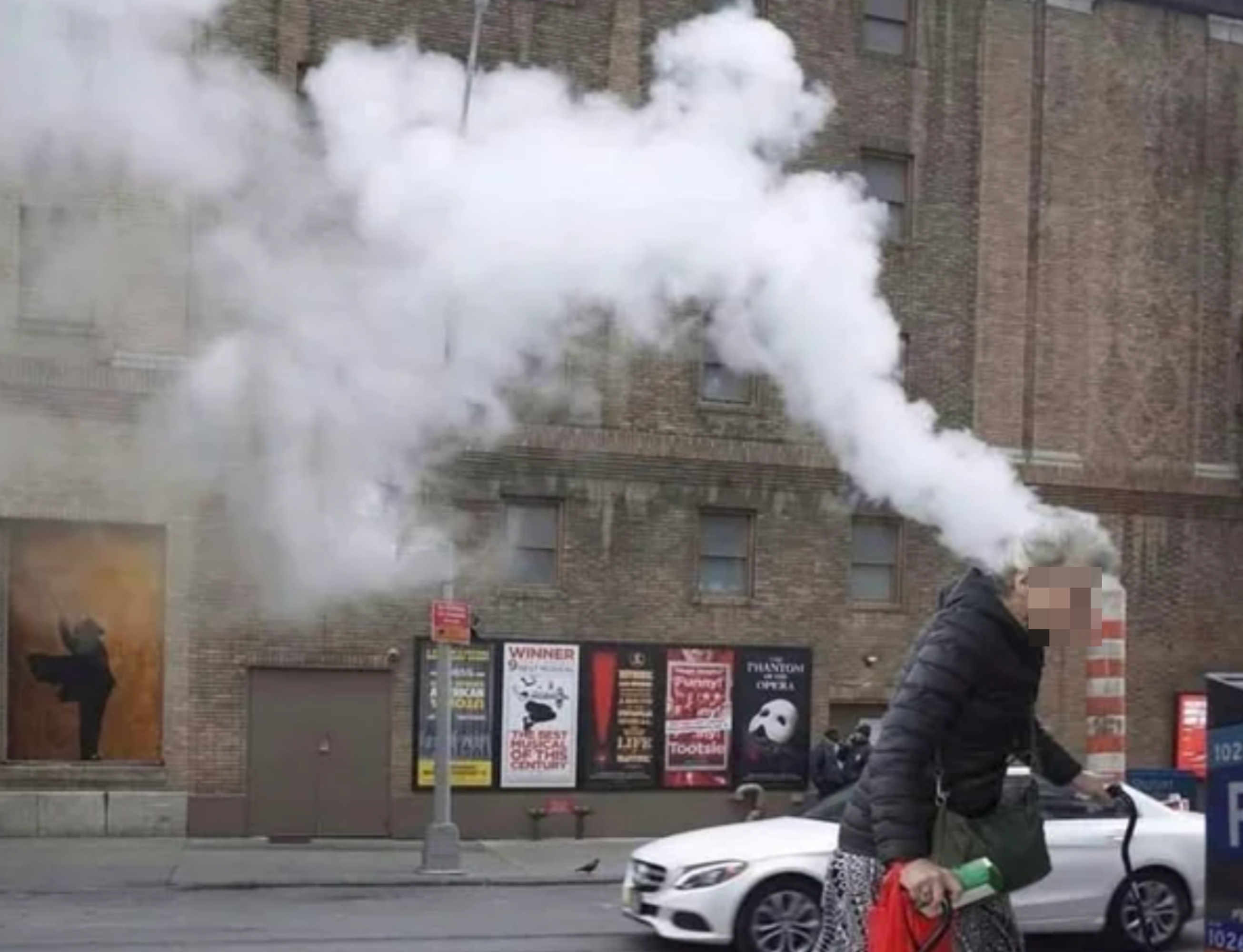 Elderly woman walks on a city street; steam creates visual illusion of smoke emanating from her head
