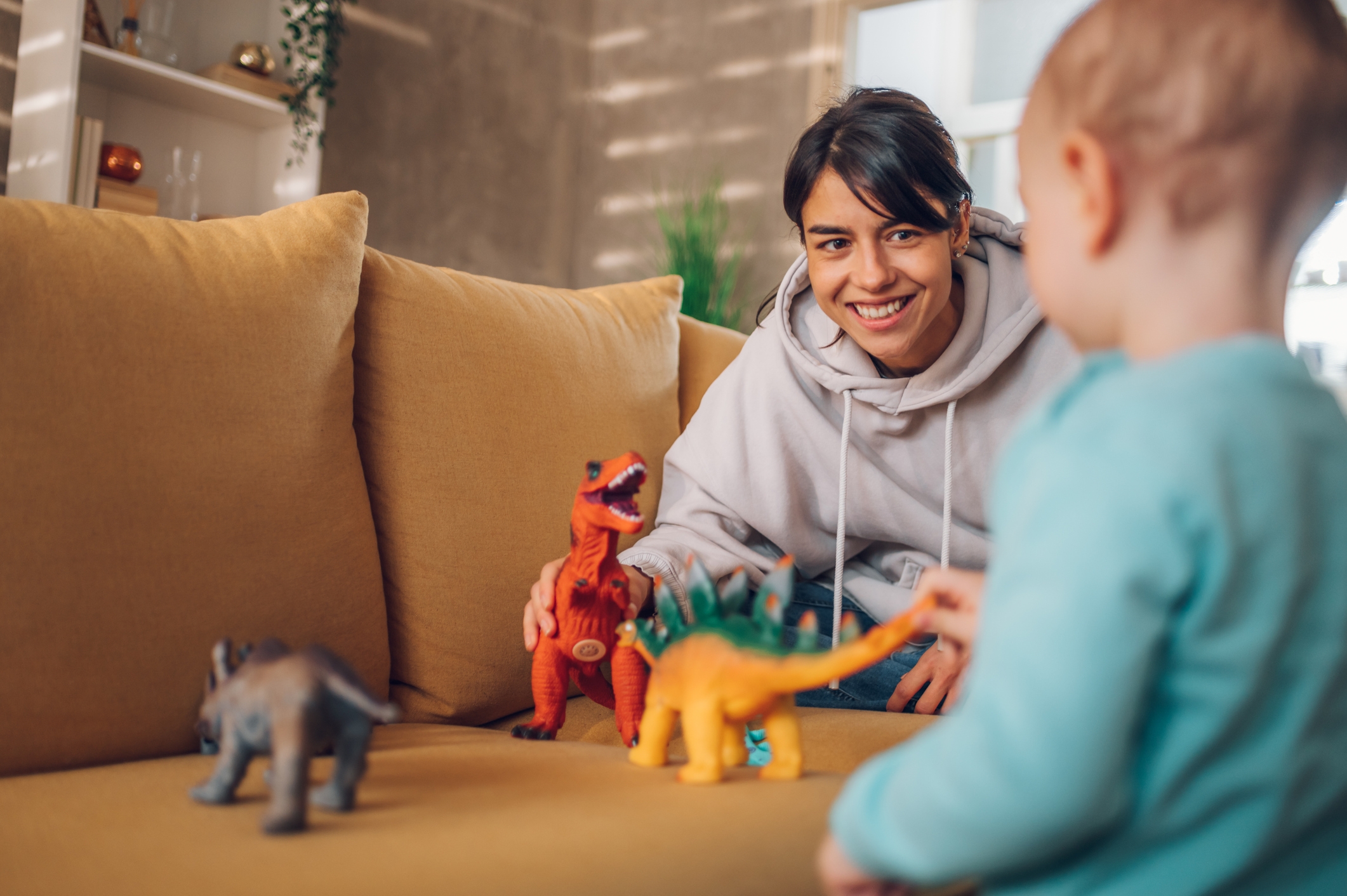 A person and a child play with dinosaur toys on a sofa, enjoying quality time together