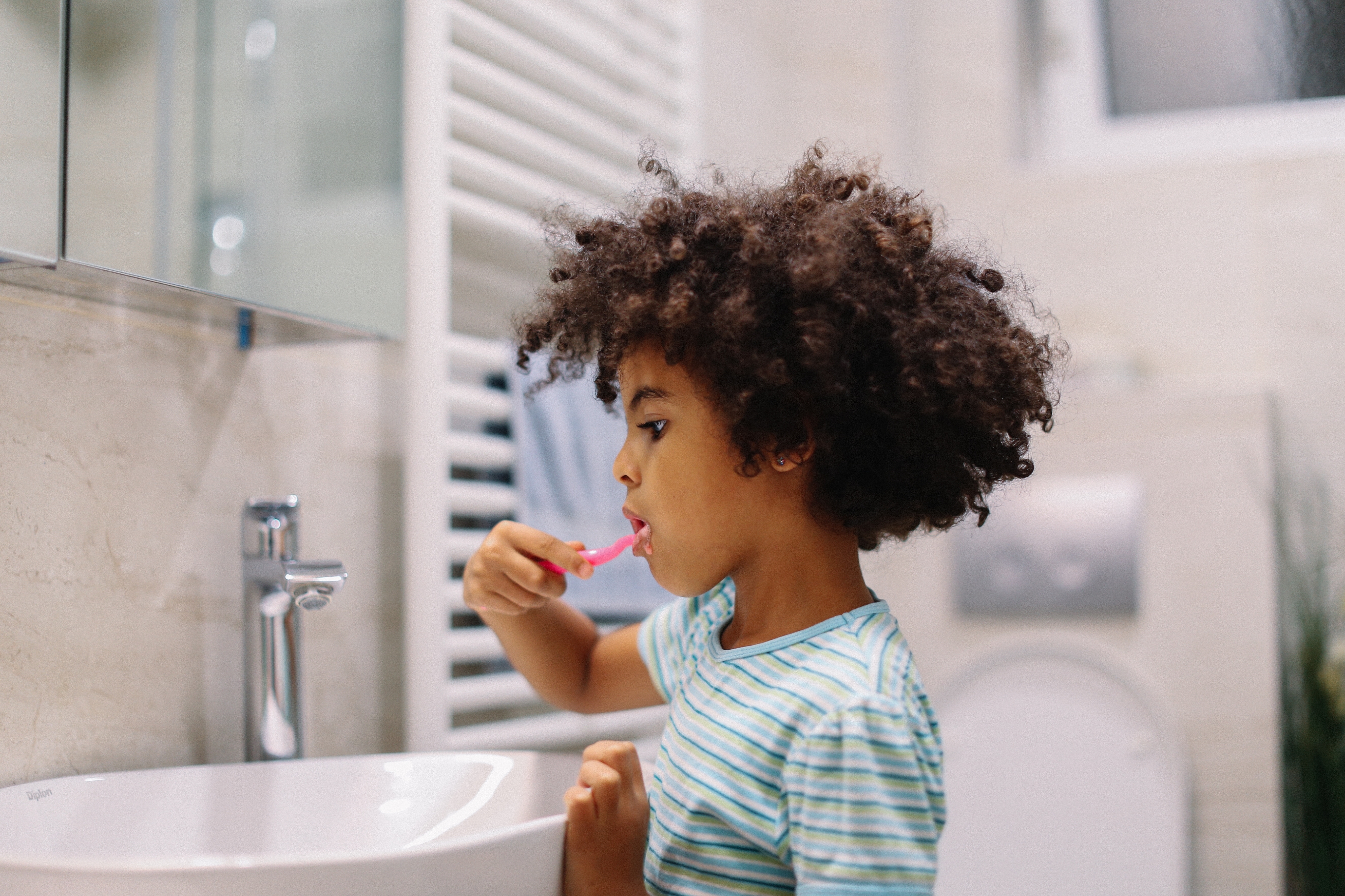 Child with curly hair brushes teeth at a bathroom sink, focusing on oral hygiene