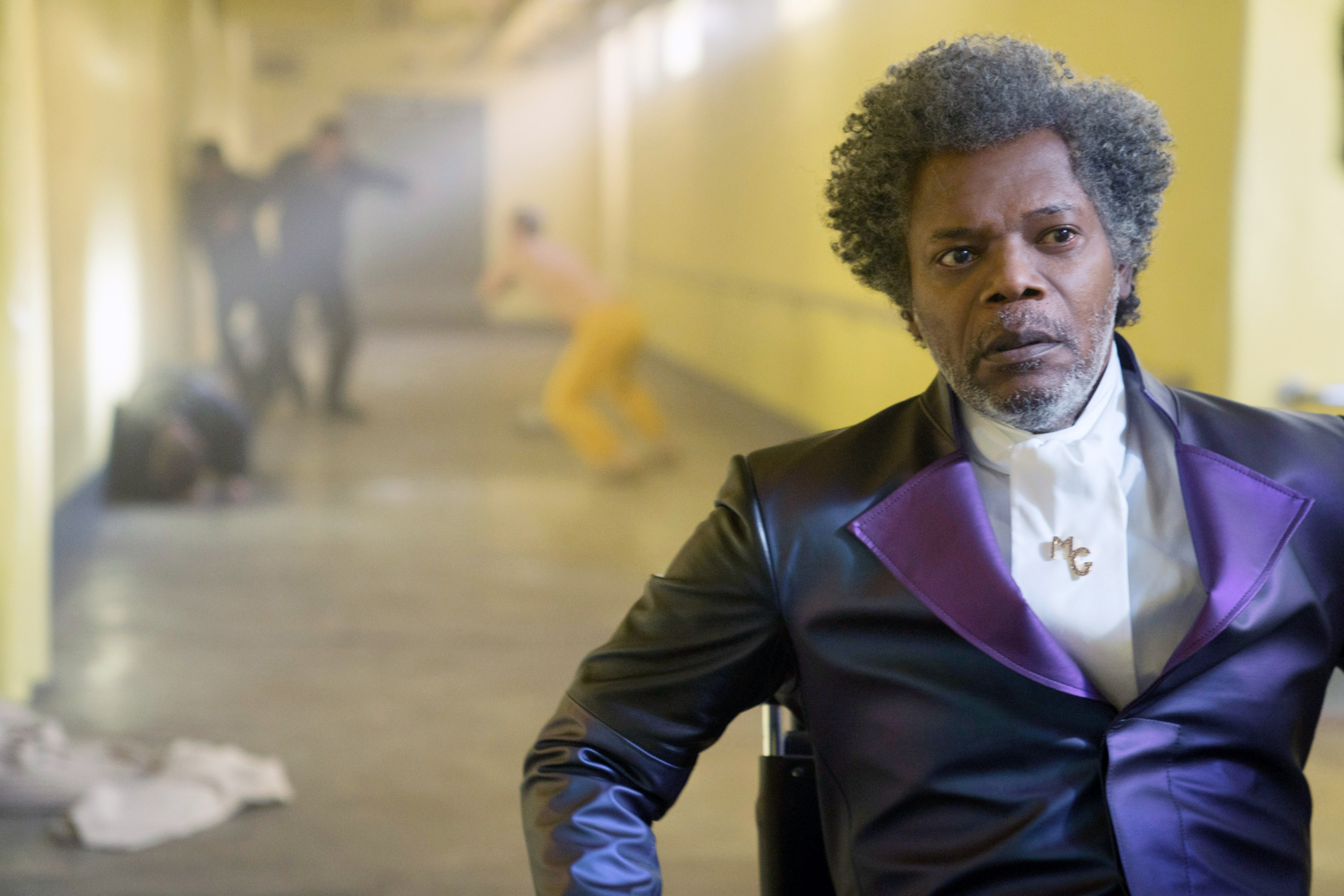 Samuel. L Jackson in a shiny, tailored suit in a hallway of people fighting