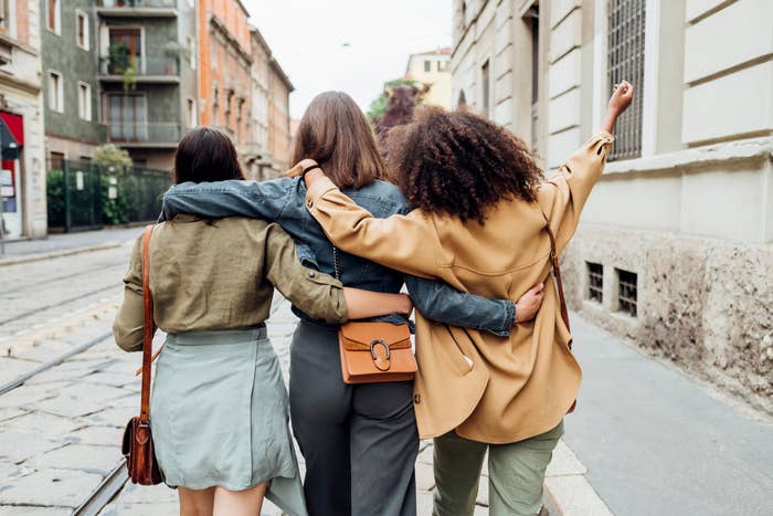 Four friends walking arm-in-arm connected  a metropolis  street, seen from behind, enjoying a casual outing together