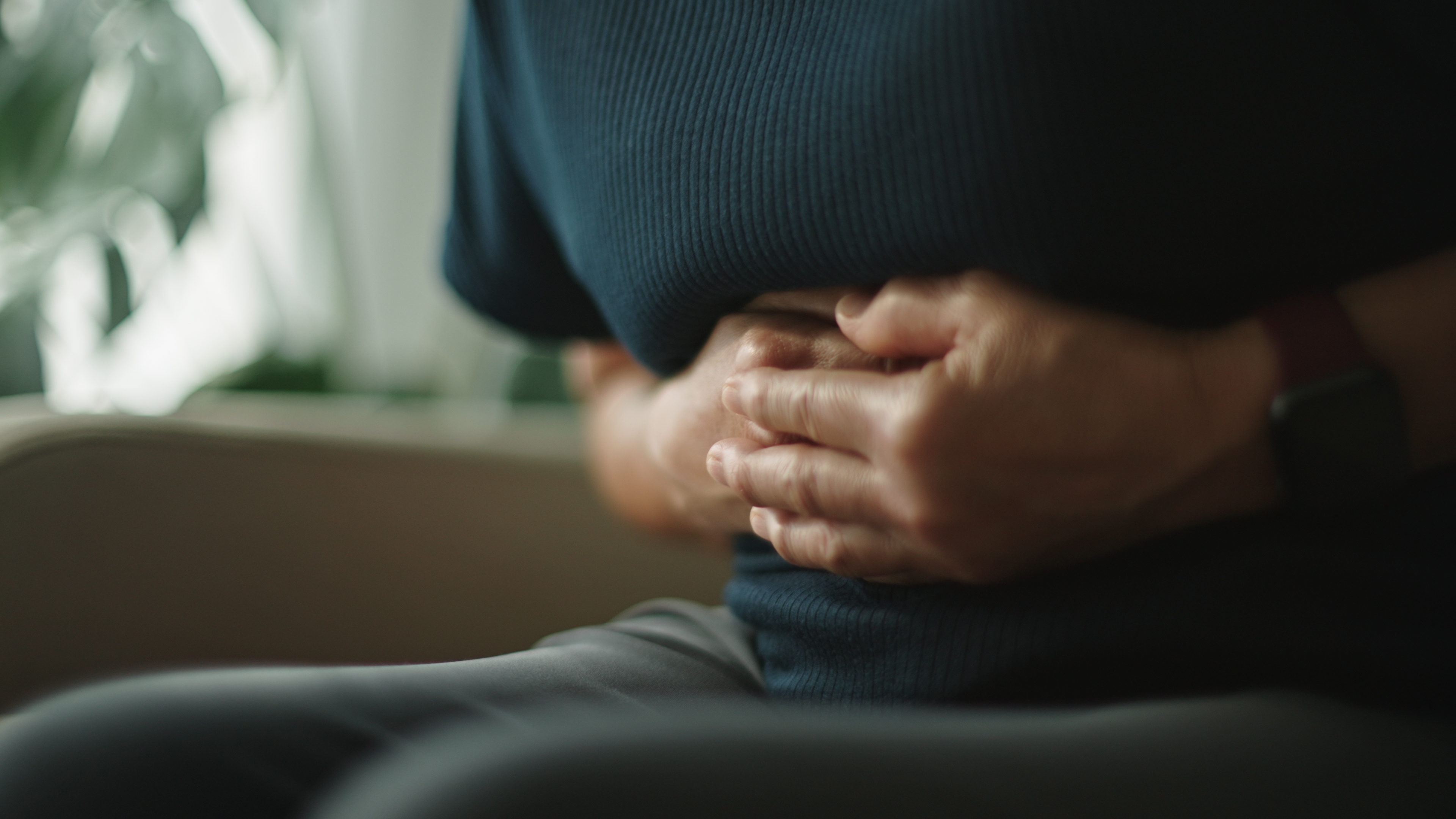 En person som sitter, klemmer magen med begge hender, noe som antyder ubehag eller magesmerter
