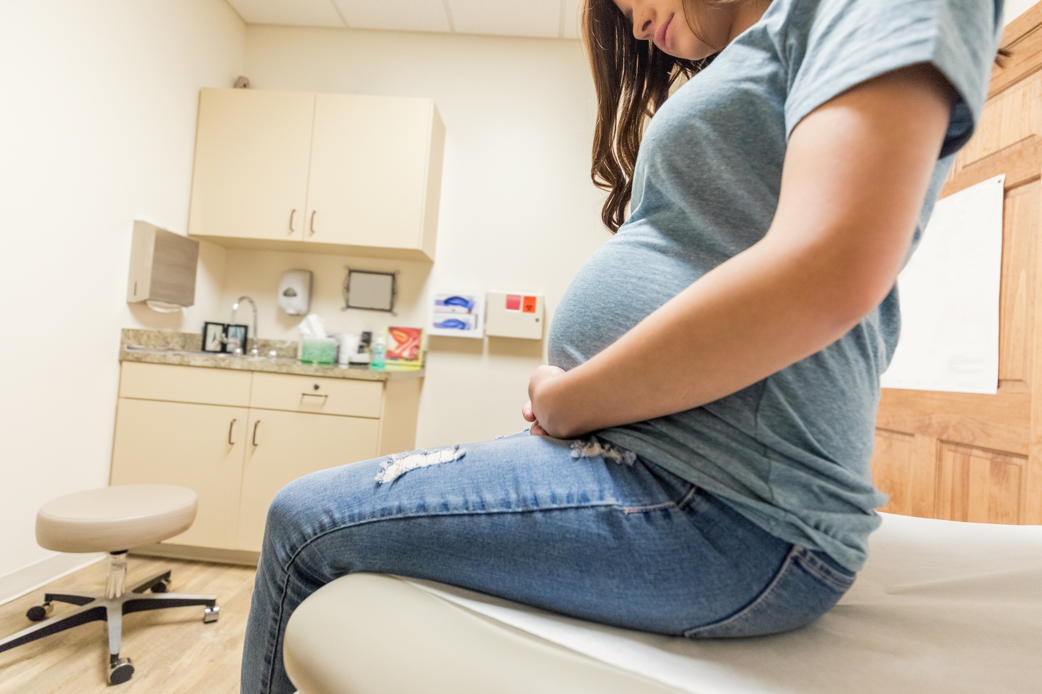 Gravid kvinne som sitter på en leges eksamensbord og holder magen forsiktig