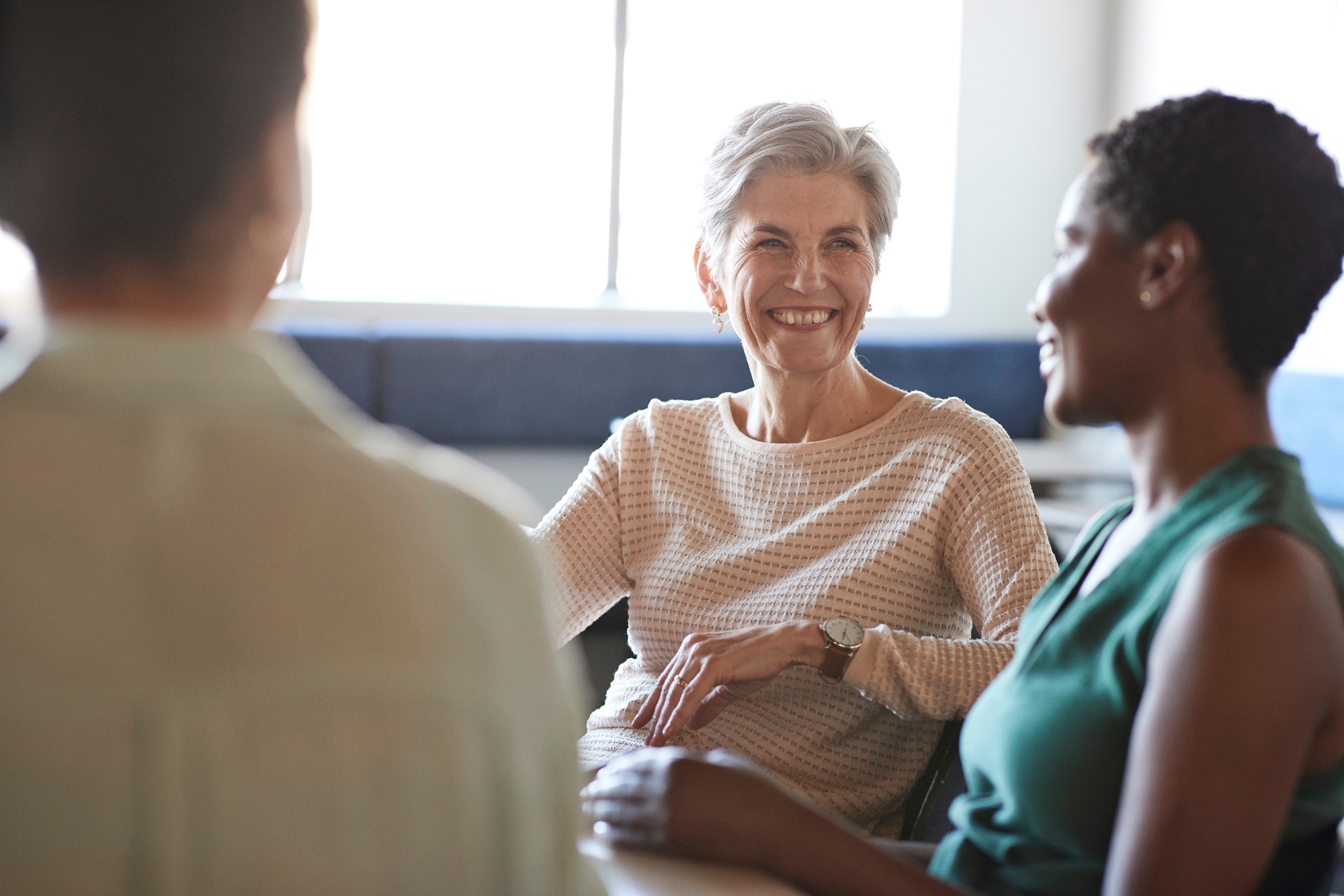 Women coworkers seated, smiling, and engaging in a friendly discussion in a bright room