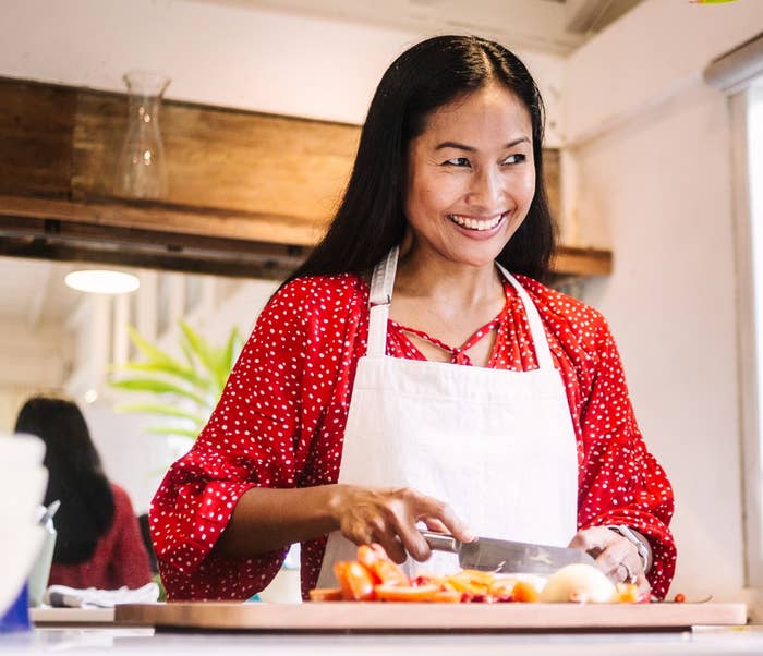 Woman in a kitchen smiles while chopping vegetables, wearing a polka dot outfit and apron