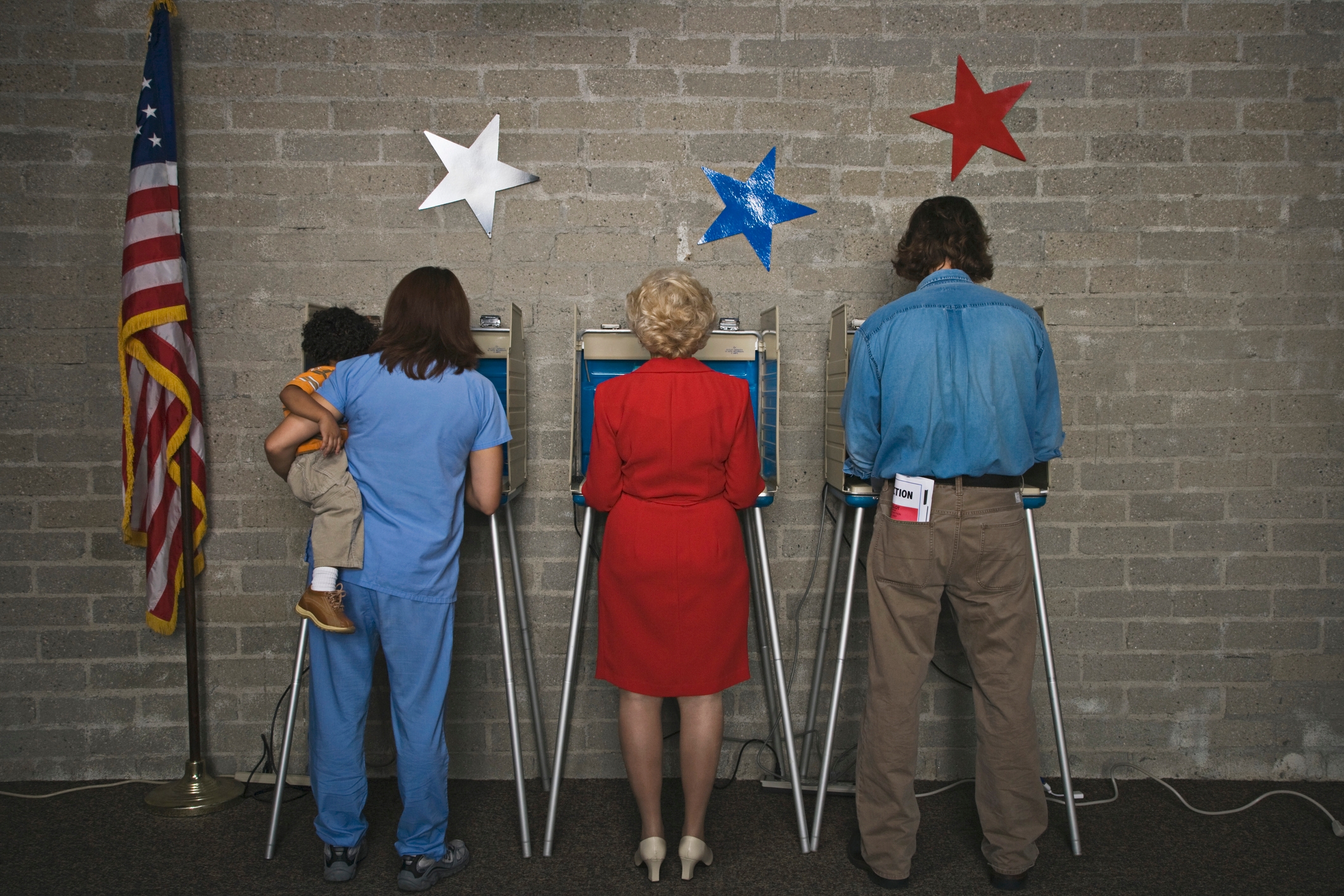 Three people voting: a parent holding a child, a person in a red dress, and another in casual attire at polling booths with star decorations