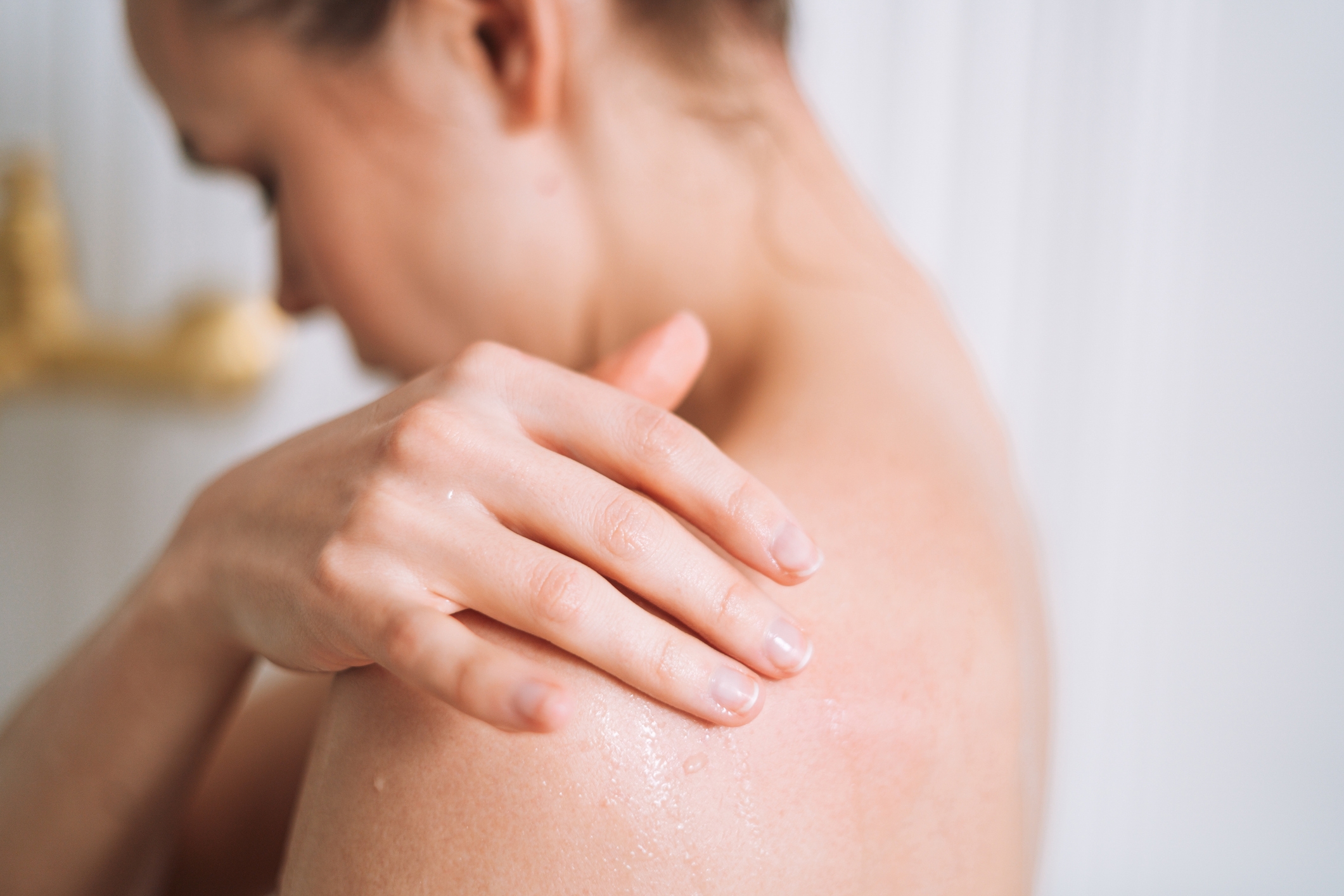 Personen som berører den fuktige skulderen sin, og bruker sannsynligvis hudpleie eller post-Shower. Fokuser på den milde, beroligende gesten