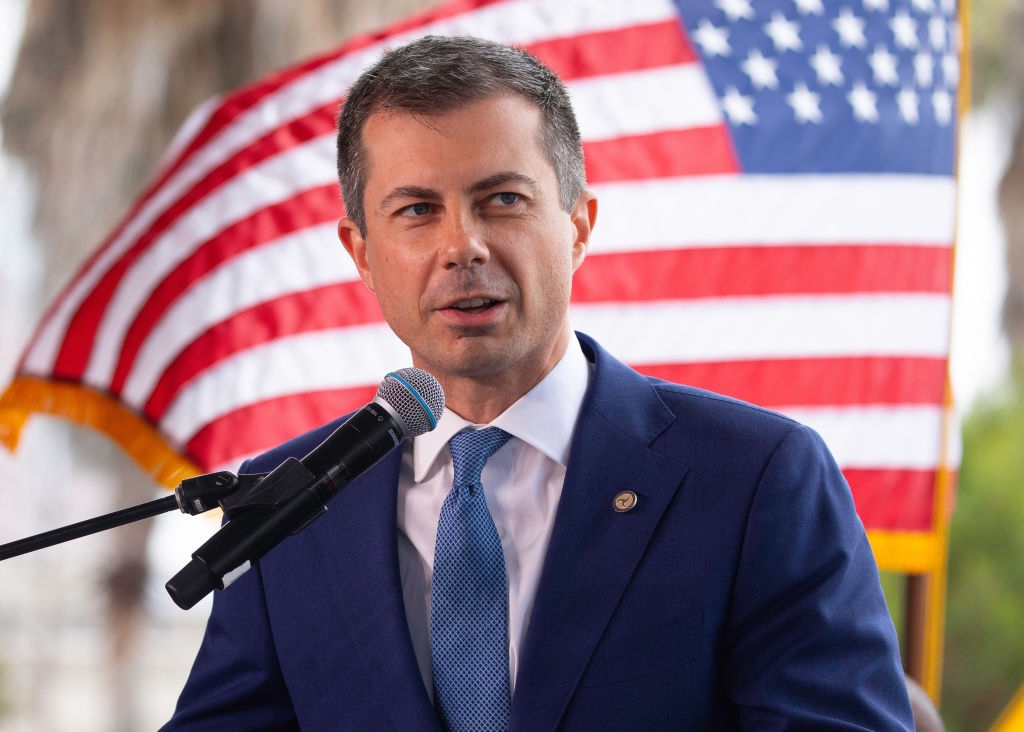 A person in a suit speaks at a podium with a U.S. flag in the background, conveying a formal or political setting