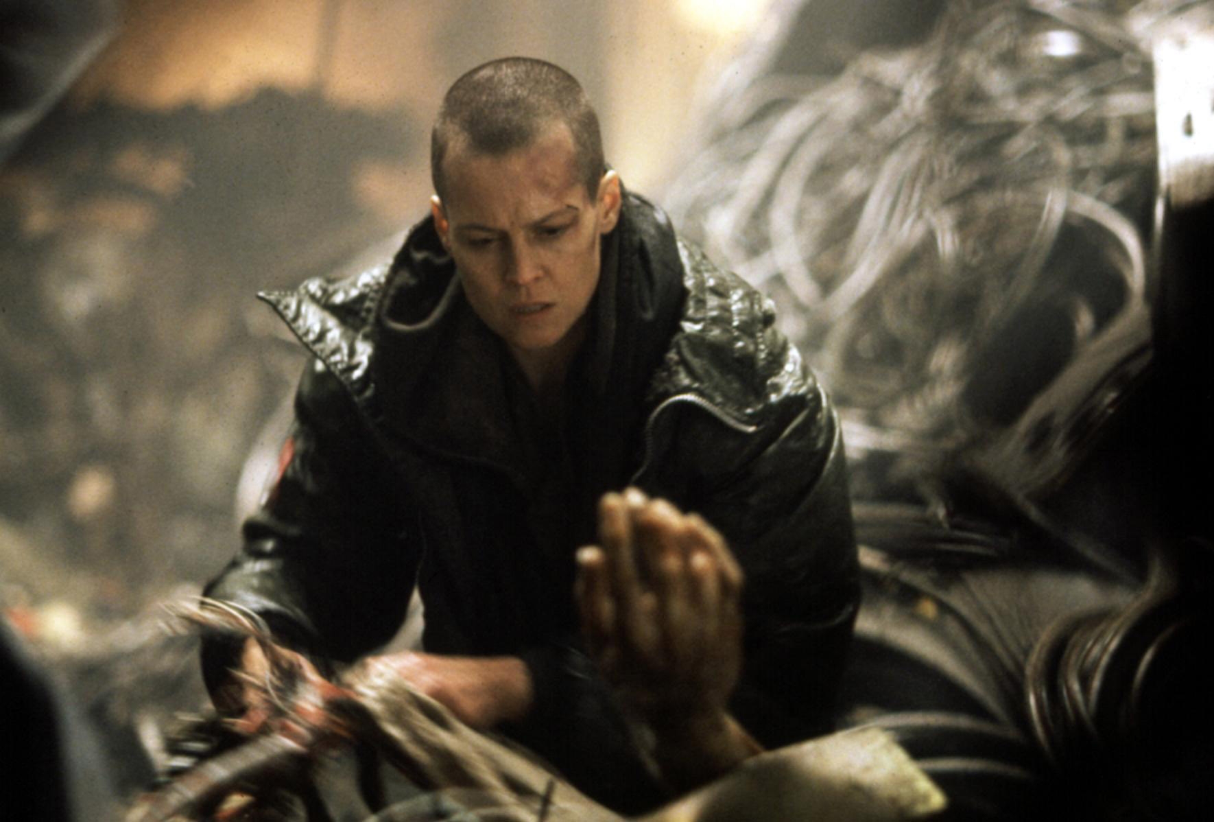 Person in a futuristic setting wearing a dark hooded jacket, appearing focused amidst complex machinery and wires