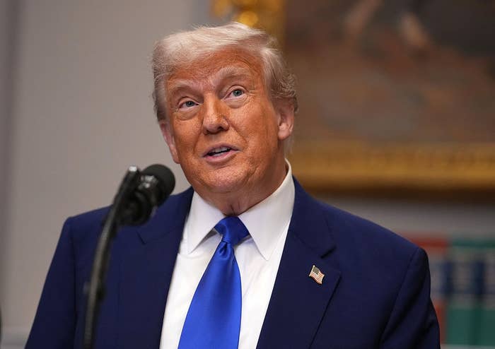 A person in a suit with a blue tie speaks at a podium, looking upwards, in a formal setting