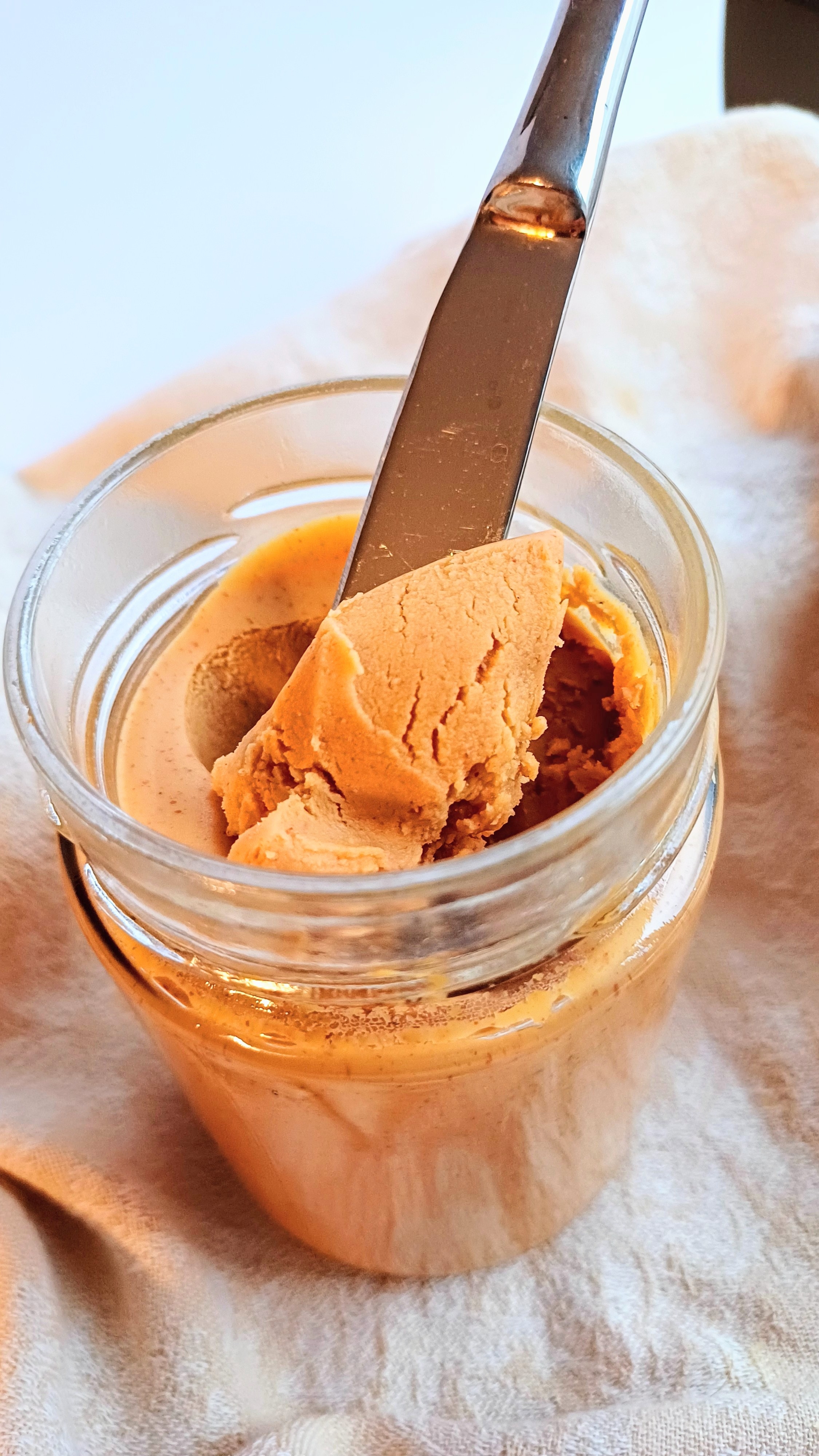 Peanut butter in a jar with a butter knife sticking into it, resting on a cloth