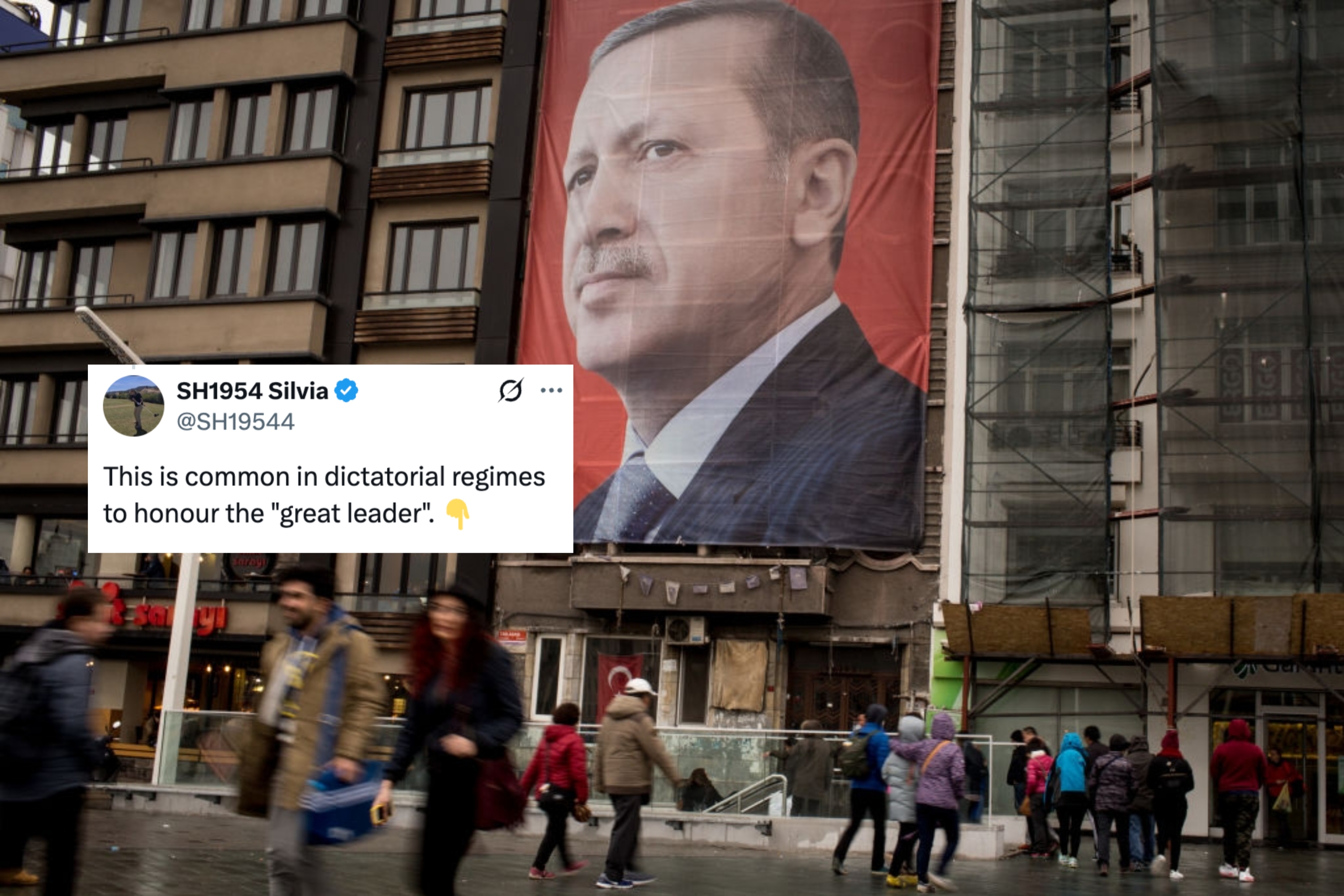 A large banner shows a man in a suit on the side of a building. People walk past on a busy street