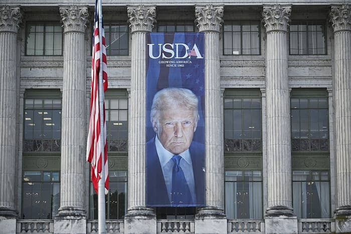 Banner with a man's face hangs on a building with "USDA, Growing America since 1862" text. Large flagpole in the foreground