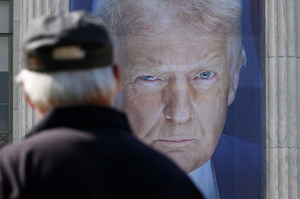 A pedestrian passes by a banner showing an image of US President Donald Trump hangs on the side of a US Department of Agriculture building in Washington, DC