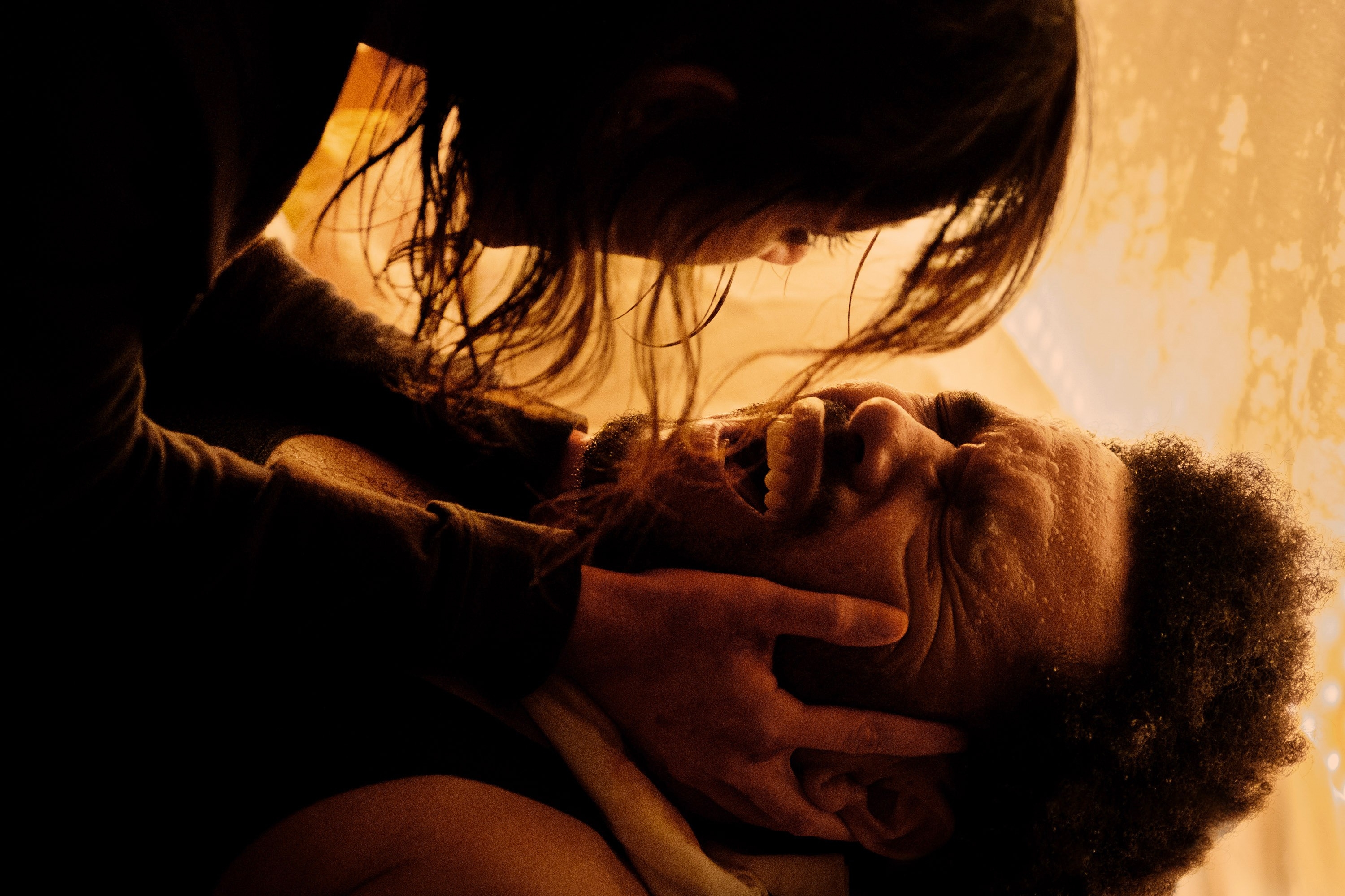 A woman holding a man's face tenderly; he appears emotional, with closed eyes and an expression of distress or contemplation