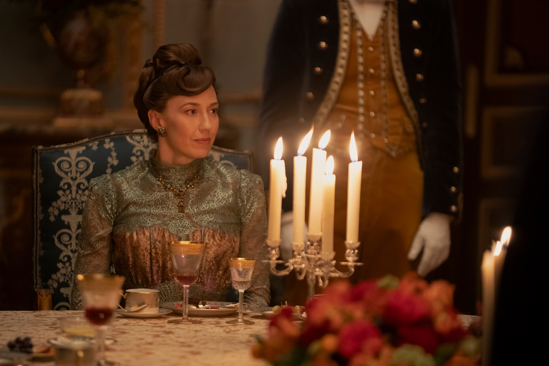 Carrie Coon in a scene from The Gilded Age sitting in a regal setting by candle light