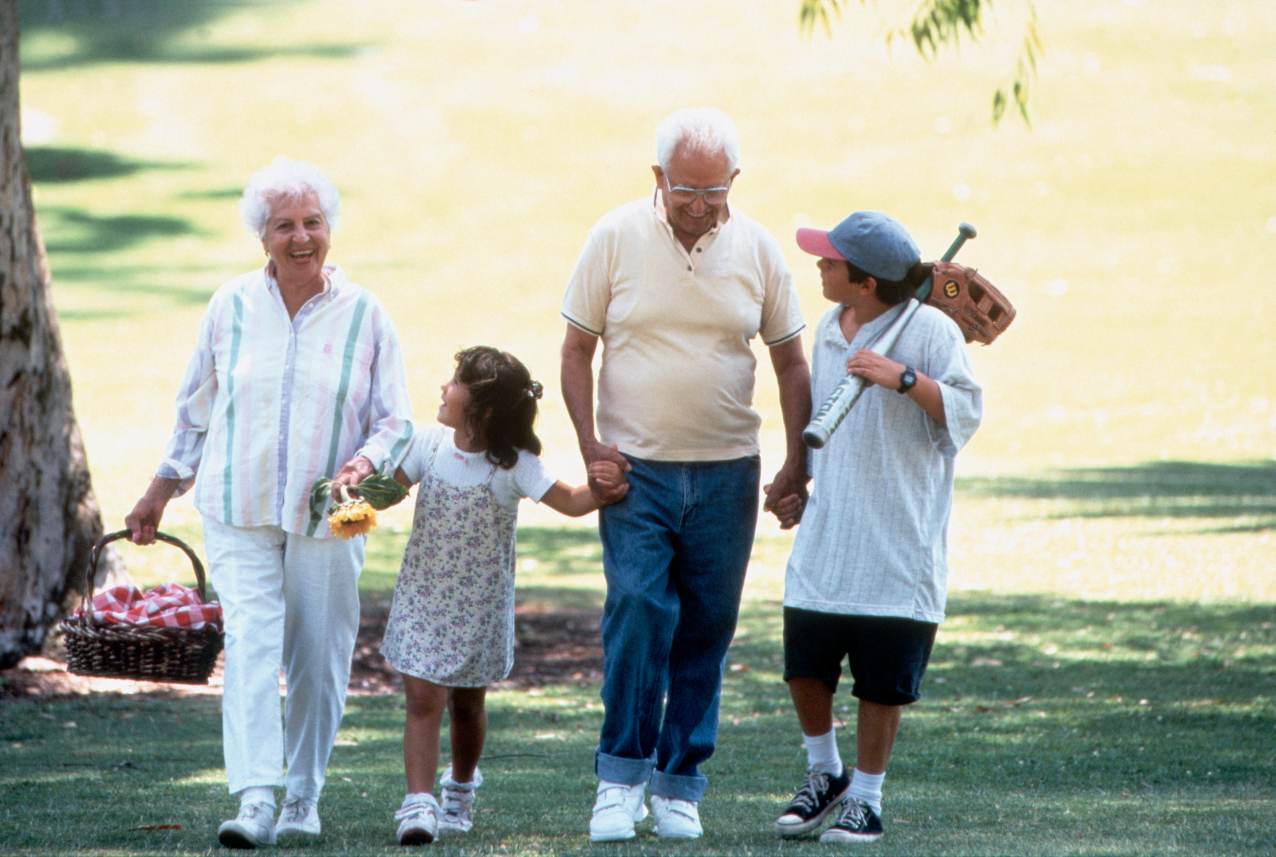 Elderly couple and two children walk in a park. The girl is holding a basket, and the boy has a toy wooden rifle over his shoulder
