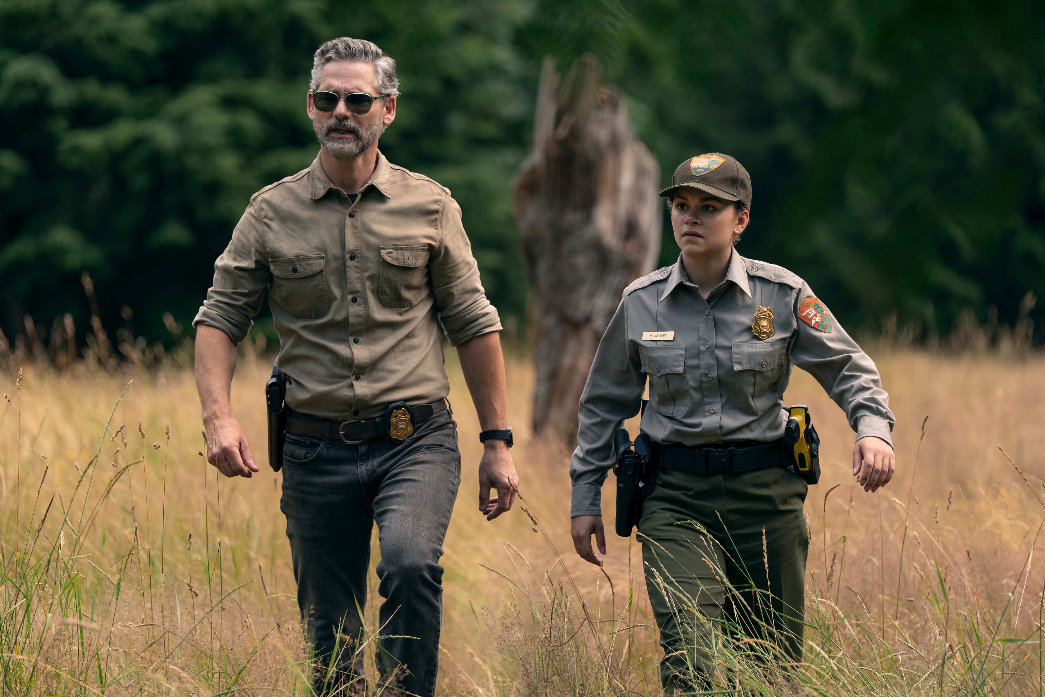 Two characters in ranger uniforms walk through a grassy field, appearing focused and serious