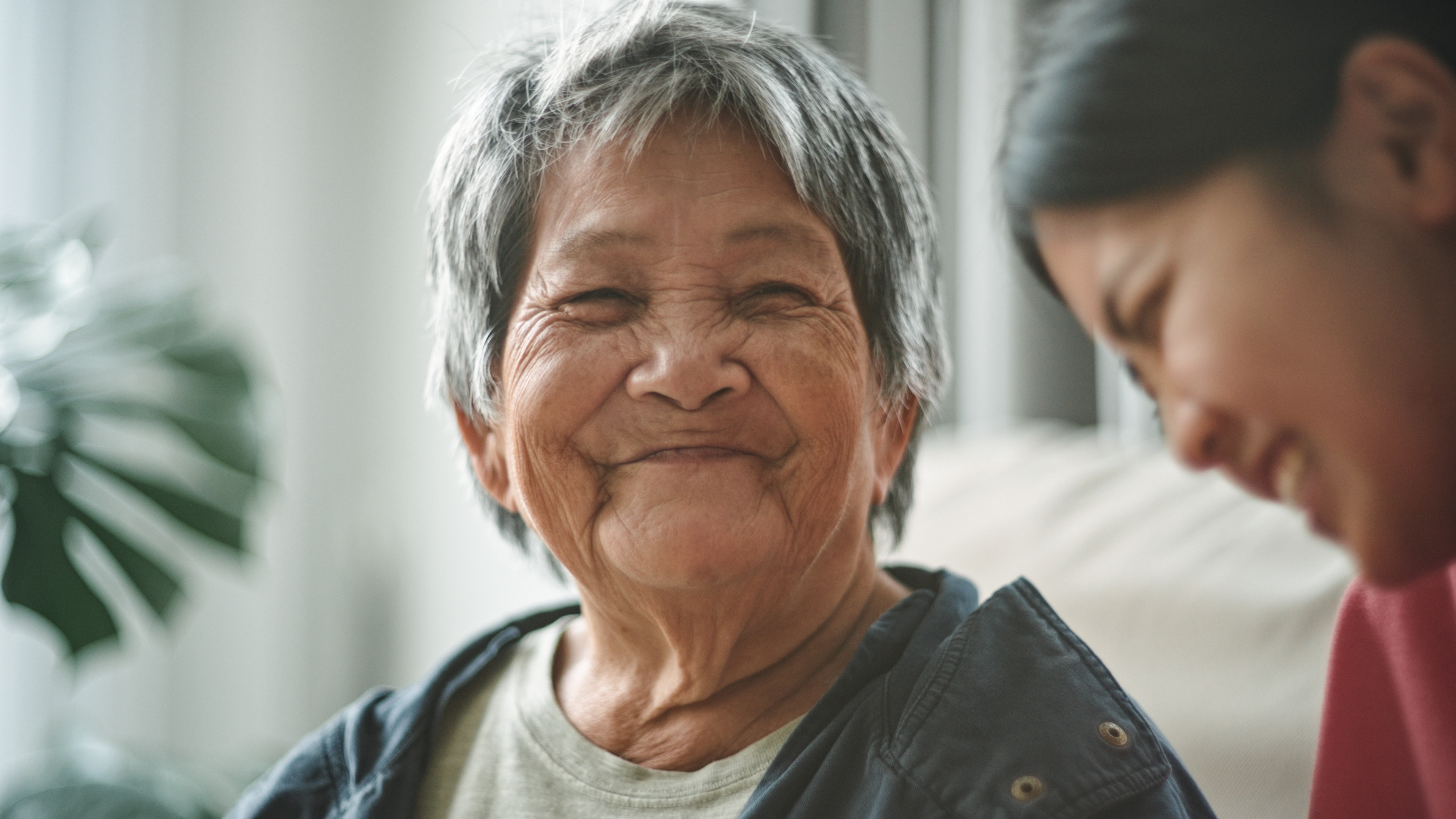 Elderly woman smiling warmly at a younger person in a cozy indoor setting, conveying a sense of warmth and connection