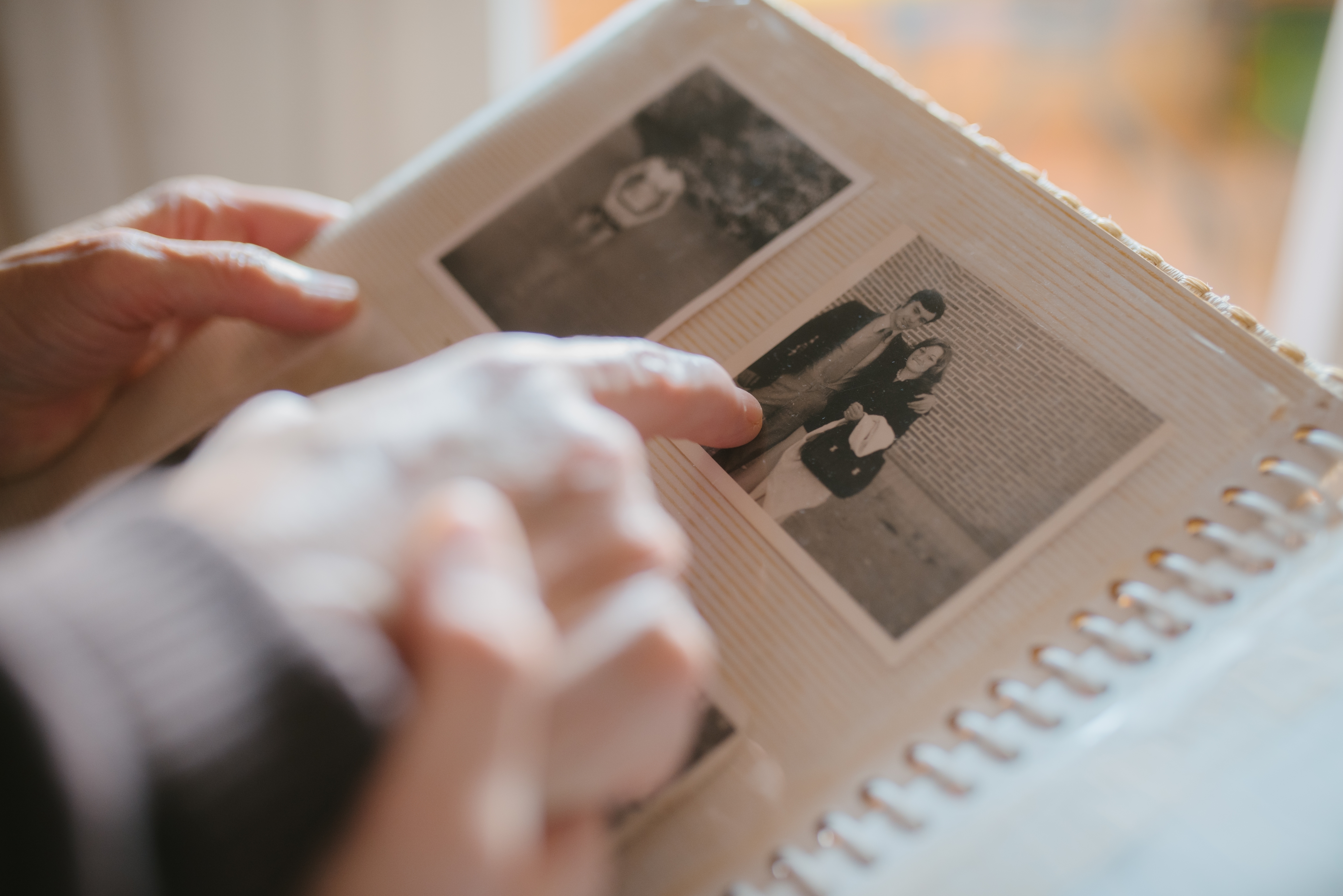 Person flipping through a photo album, pointing at a black-and-white picture of a couple posing against a brick wall