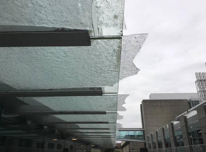 Damaged glass canopy with shards missing above a modern building's entrance walkway