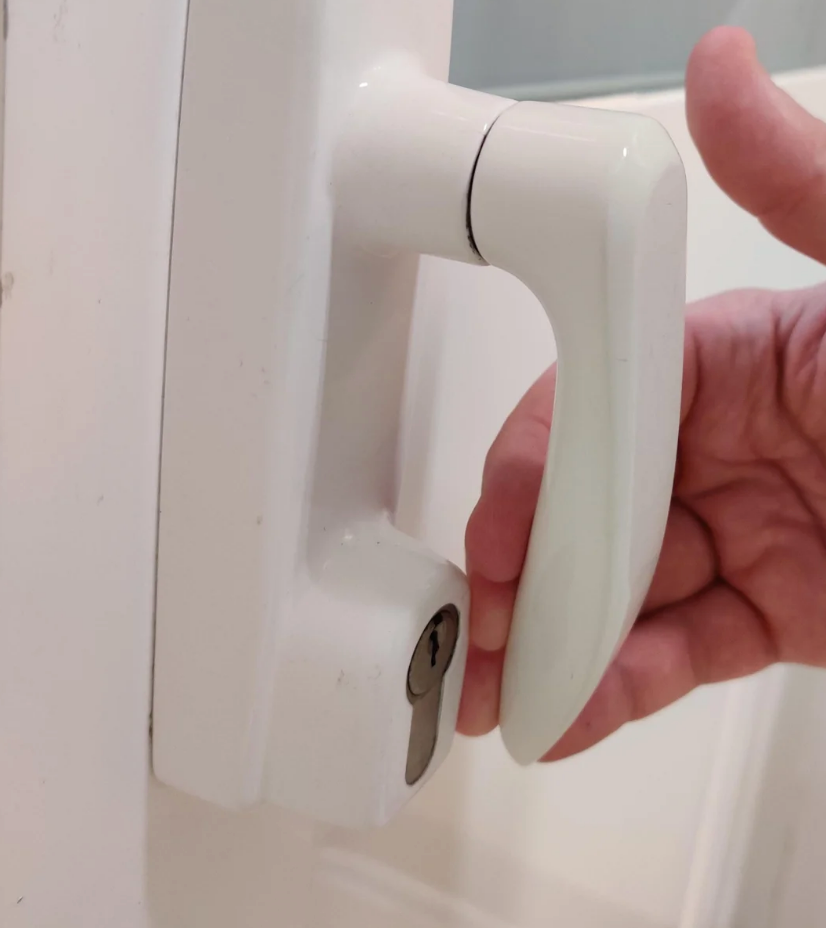 A hand turning a white door handle with a keyhole below