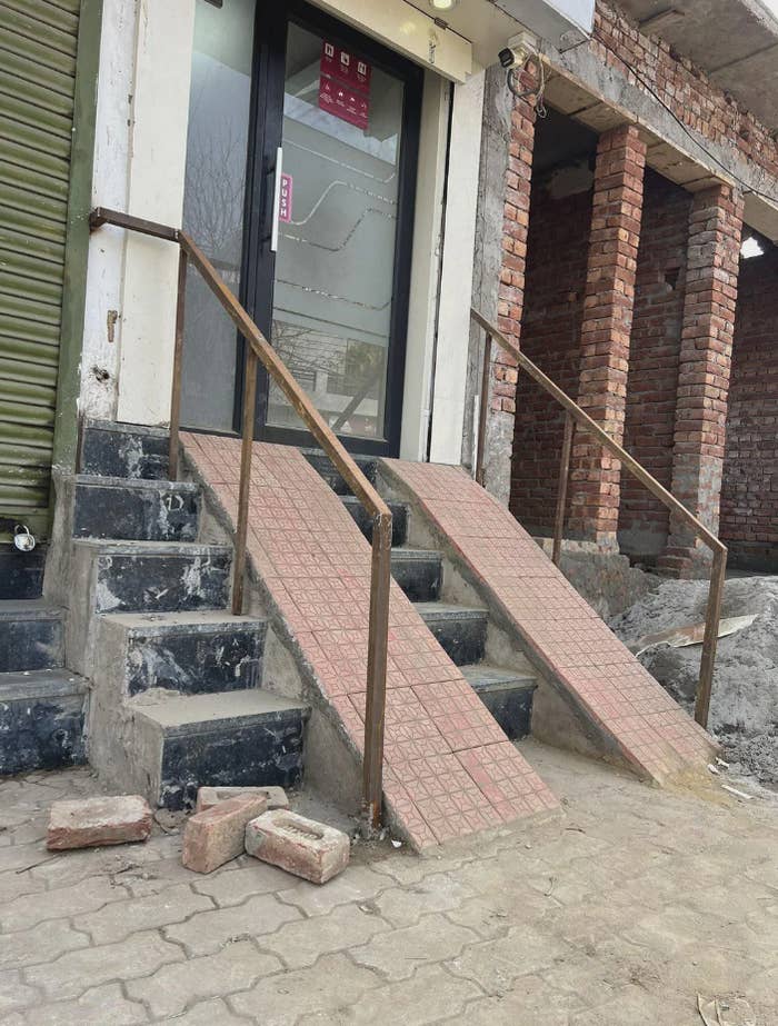 Building entrance with stairs and two ramps with steep angles. Some bricks are on the ground nearby