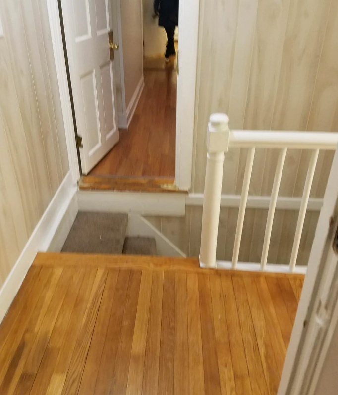 Staircase leading to a lower hallway. Partially open door at hallway end. Careful navigation needed due to an uneven step