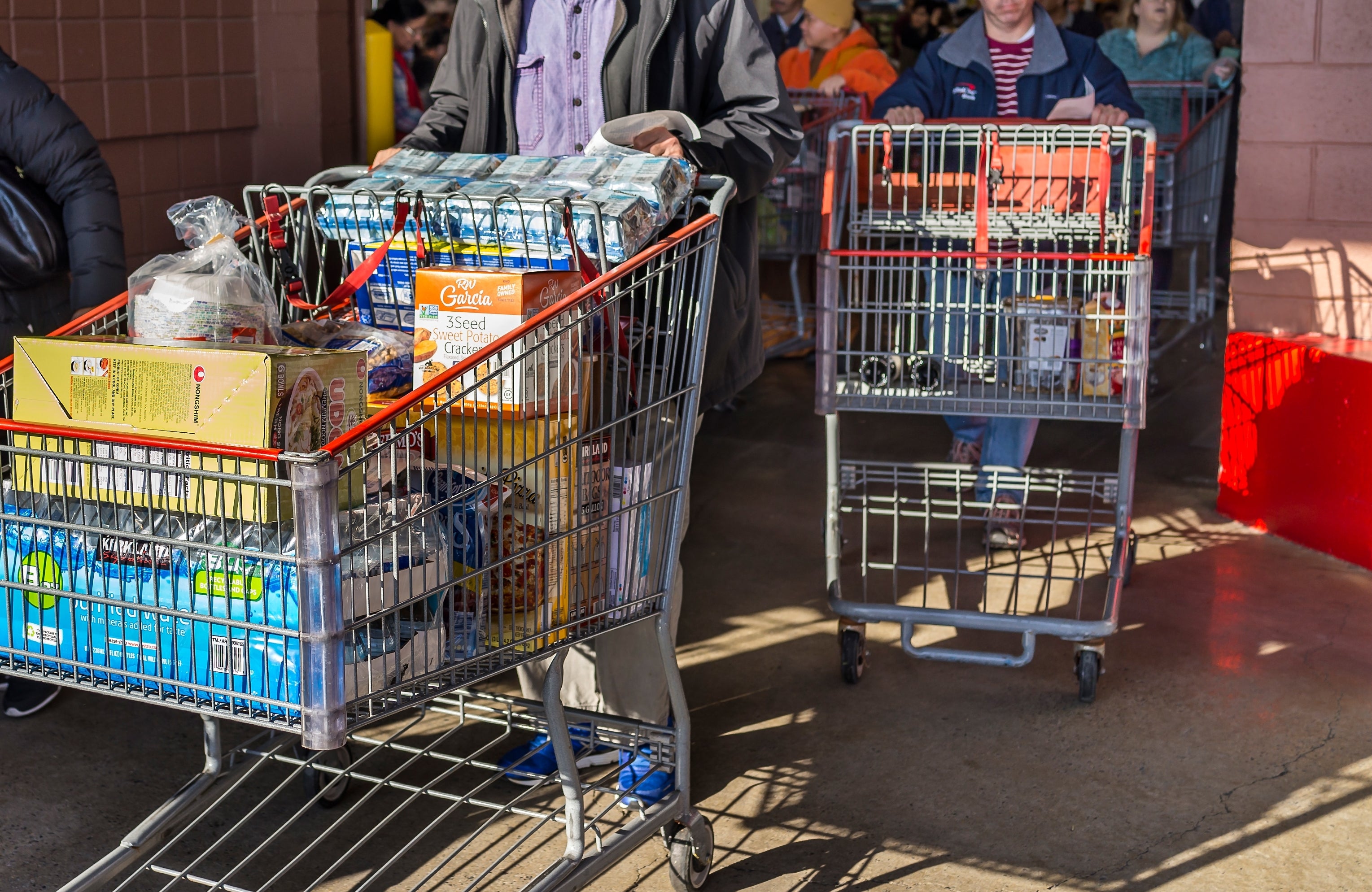 People pushing shopping carts filled with groceries, standing in line at a store exit