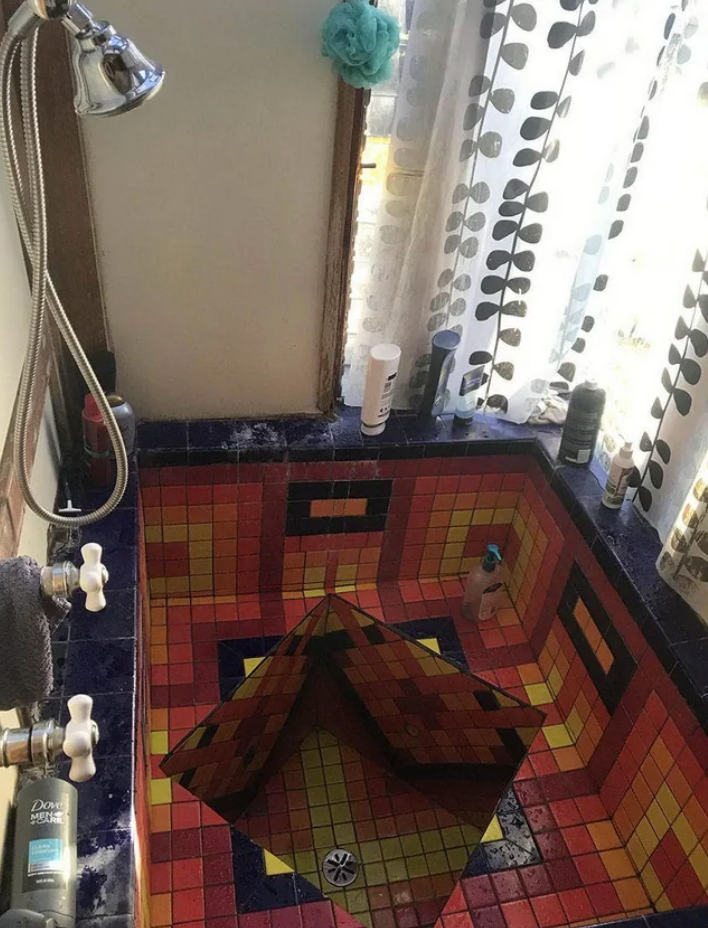 Tile shower room with geometric pattern and various toiletry bottles on ledges; curtain with leaf pattern partially drawn