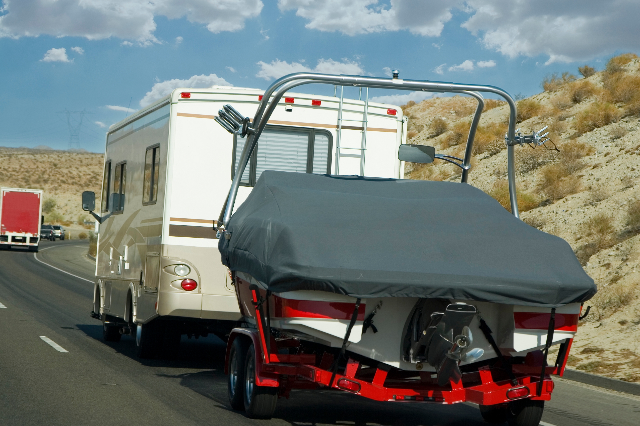 RV towing covered boat on highway in desert landscape