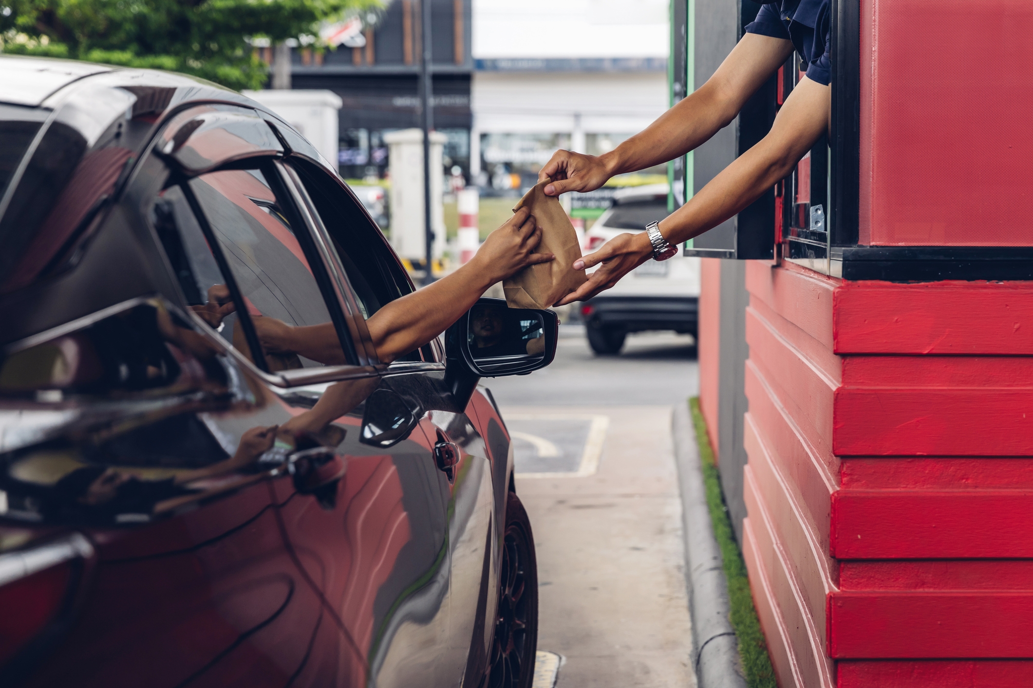 Person receives a brown paper bag at a drive-thru window from an attendant, showcasing a typical fast-food transaction