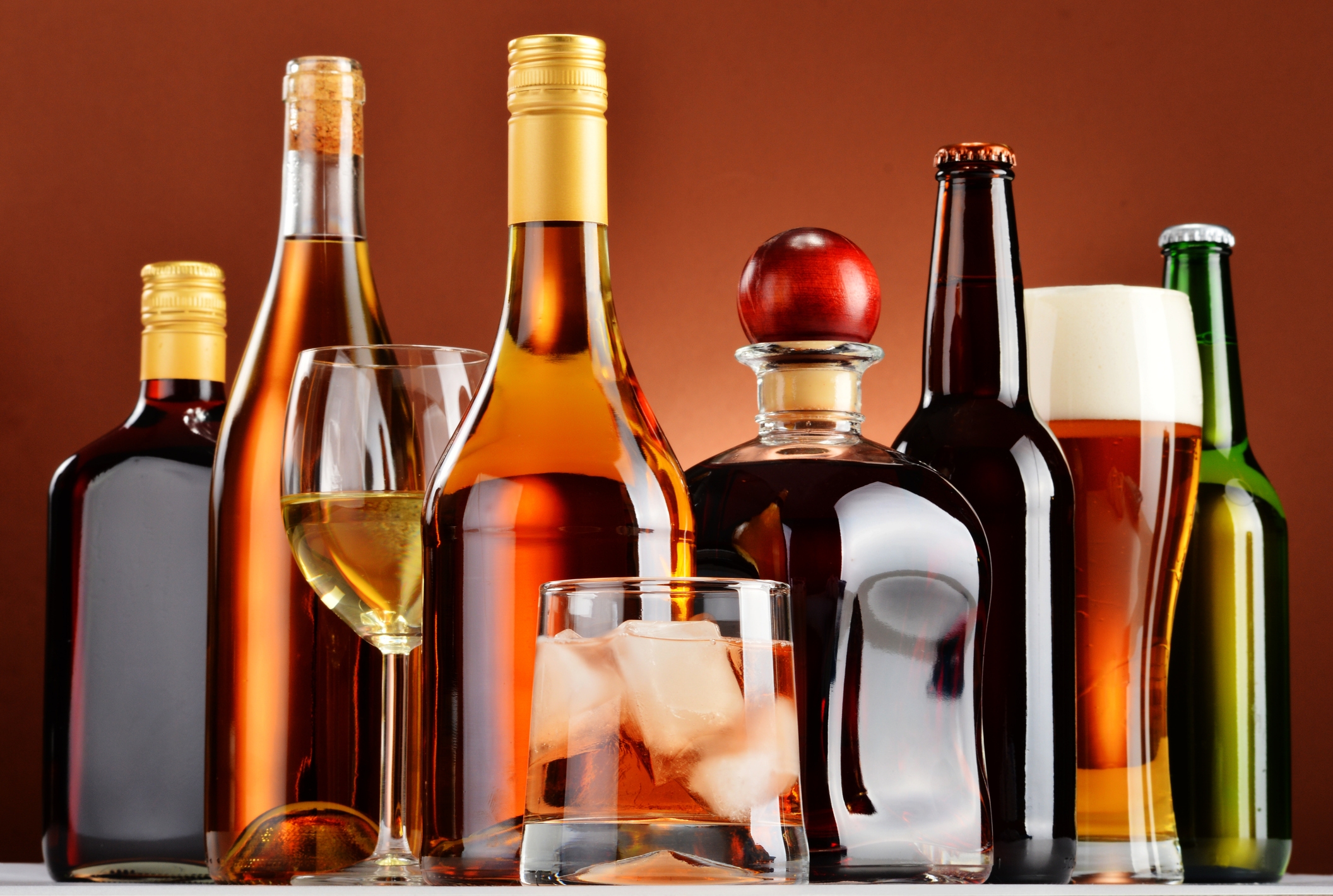 A selection of various alcoholic beverages, including wine, whiskey, and beer, displayed on a reflective surface, suggesting themes of consumption and luxury