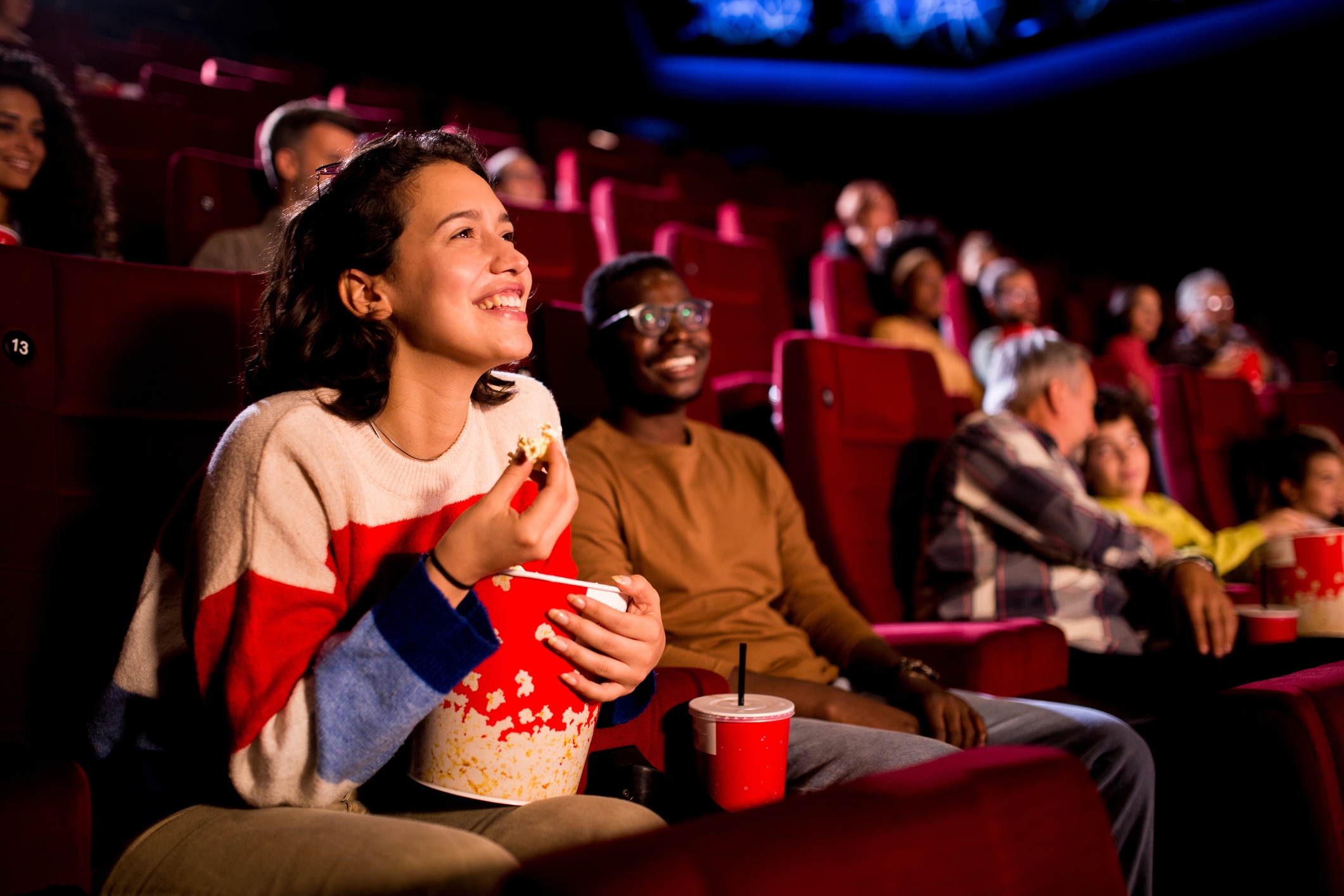 People in a movie theater enjoying snacks and watching a film with big smiles, illustrating a leisure activity related to work-life balance