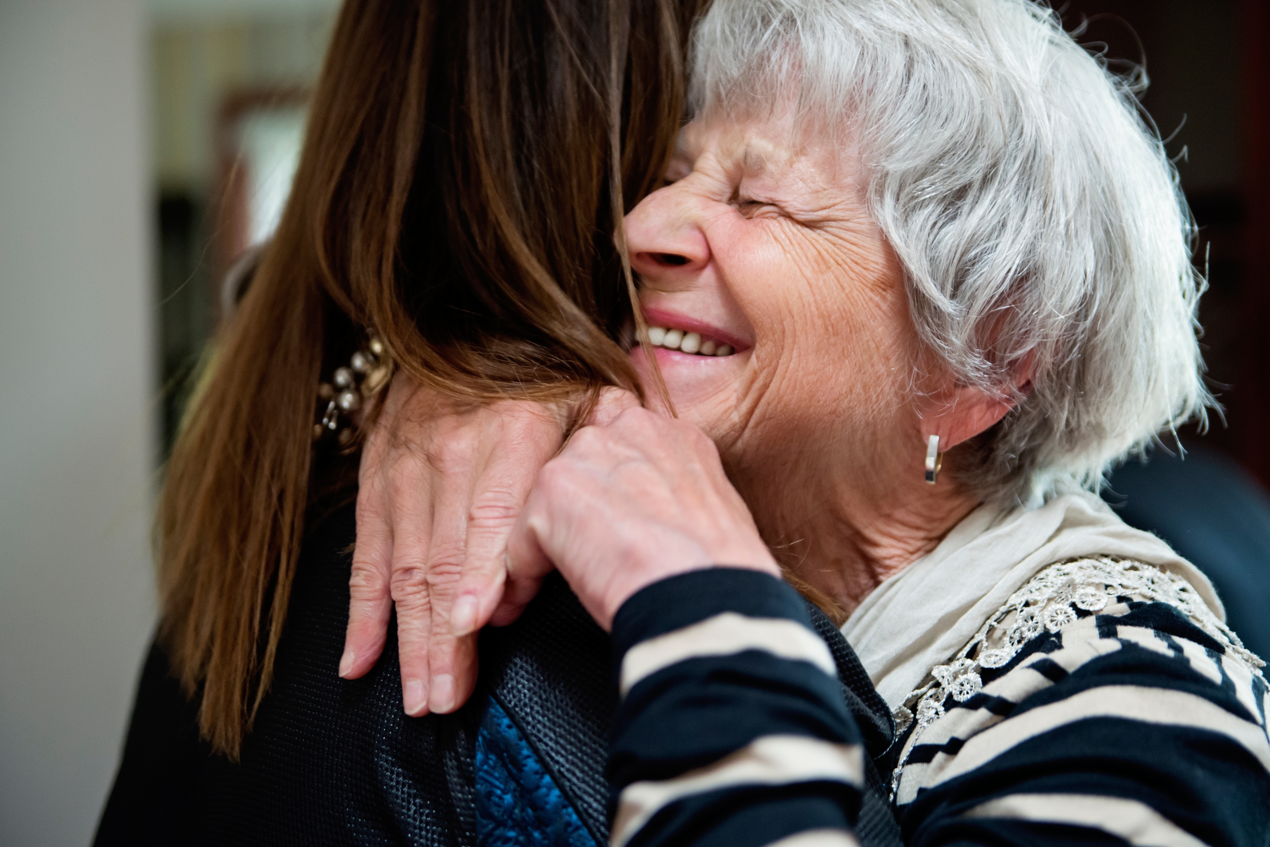 An elderly woman joyfully hugs a younger person, both smiling warmly, conveying a sense of love and connection
