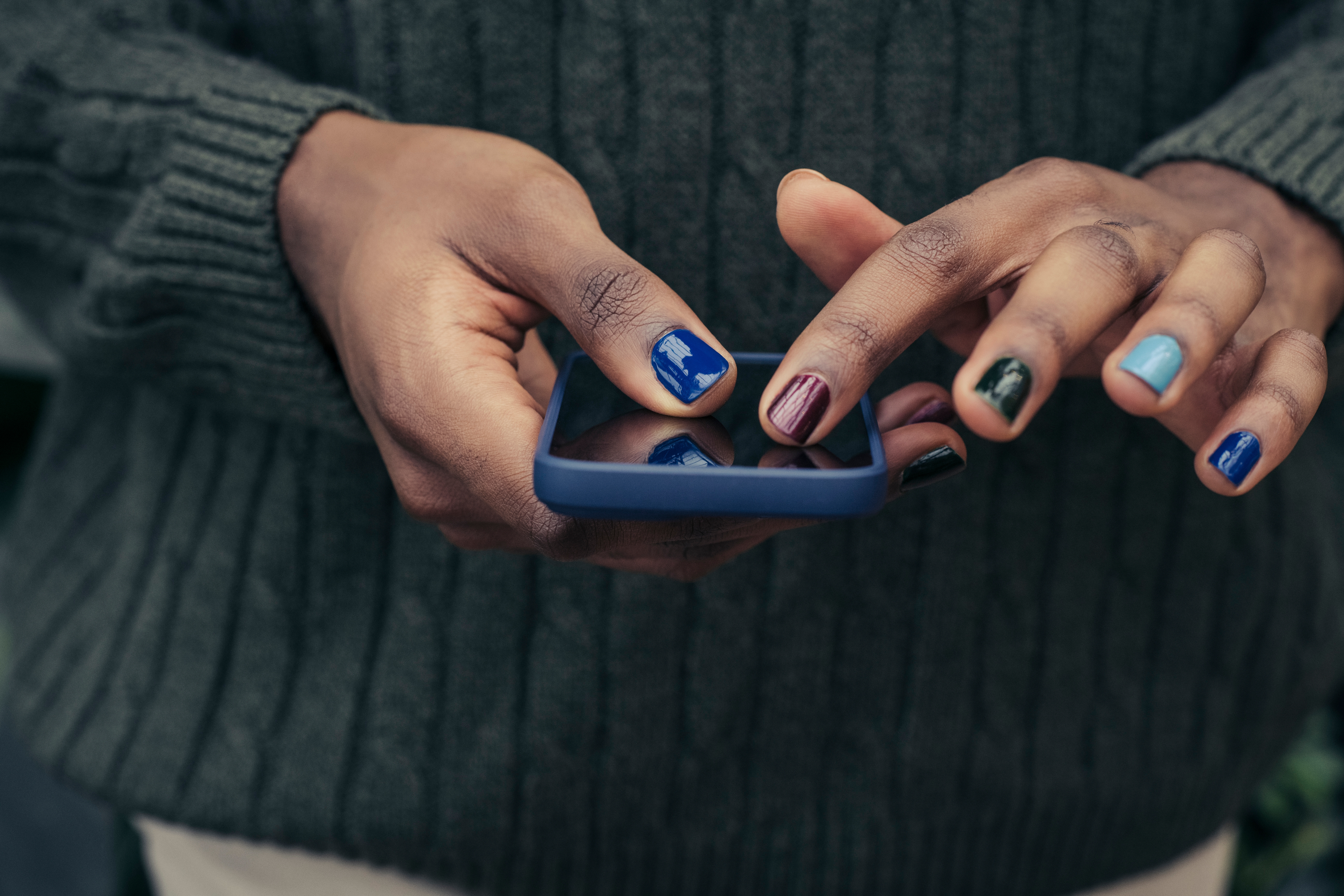 Close-up of hands with stylish painted nails using a smartphone, wearing a knitted sweater