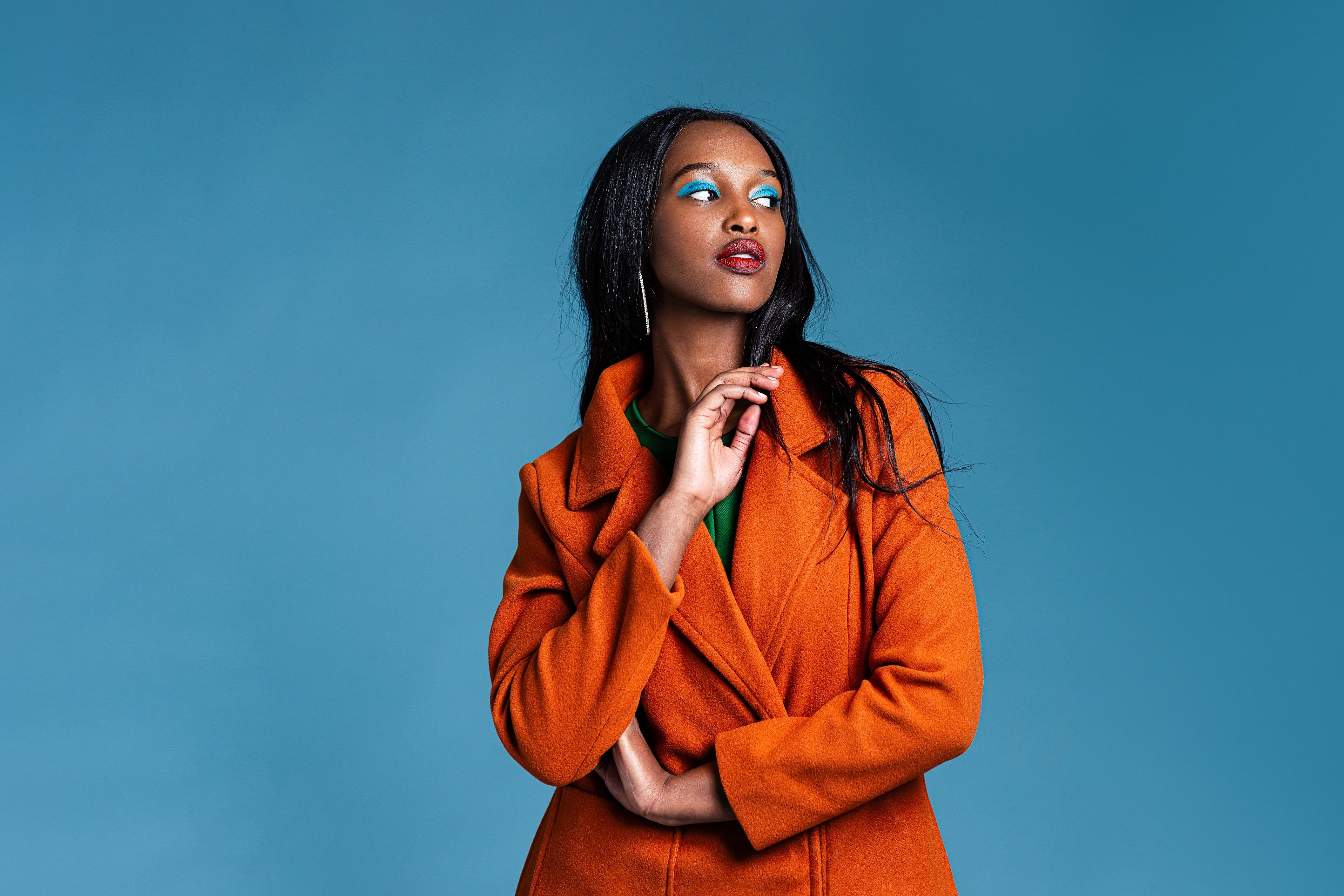 Person in a stylish coat poses against a plain backdrop, gazing confidently sideways