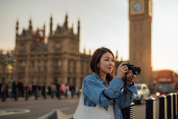 Person taking a photo near a historic clock tower in a busy city area, capturing the essence of travel and exploration