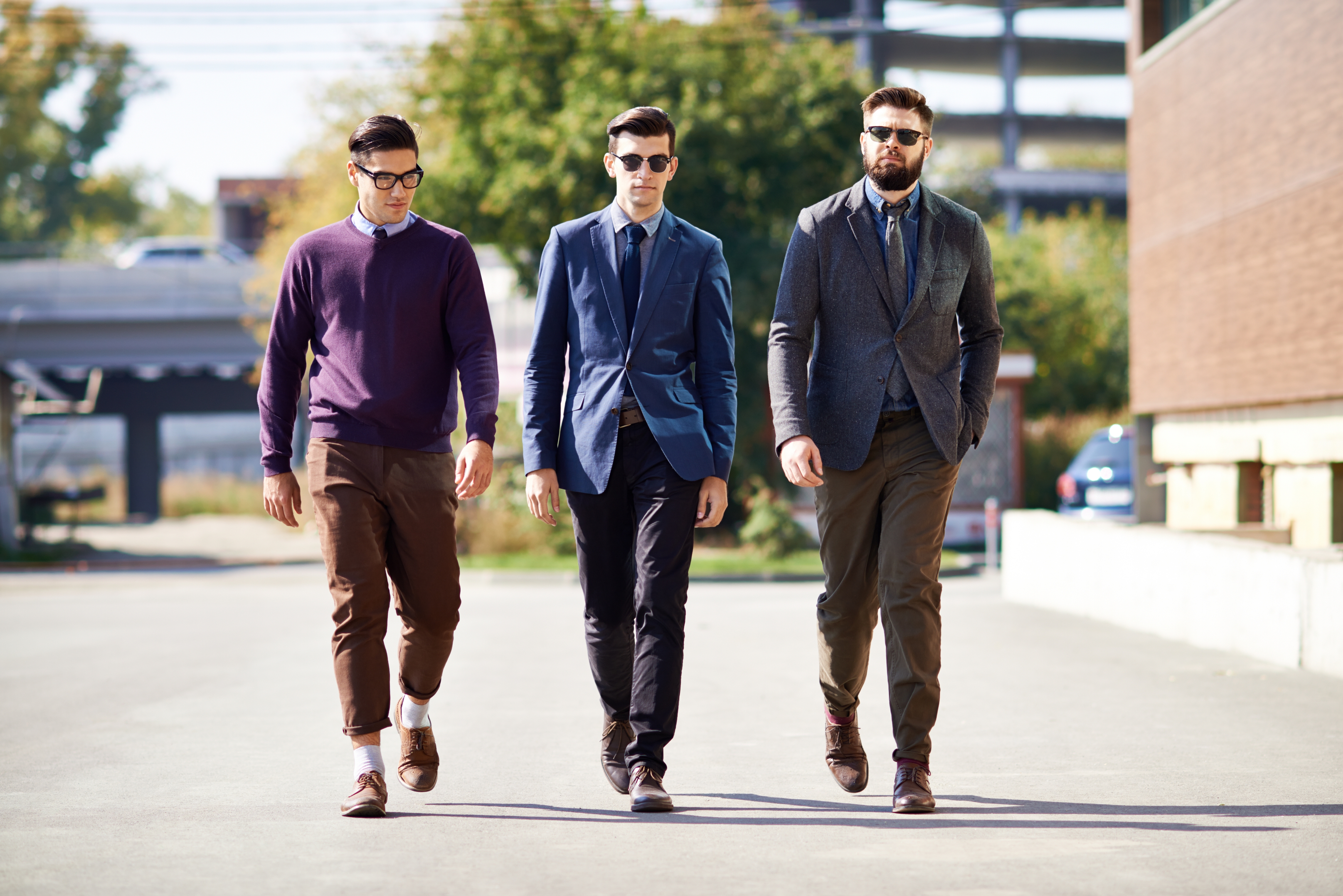 Three men walking outdoors in stylish casual and business attire, including blazers and sunglasses, on a sunny day