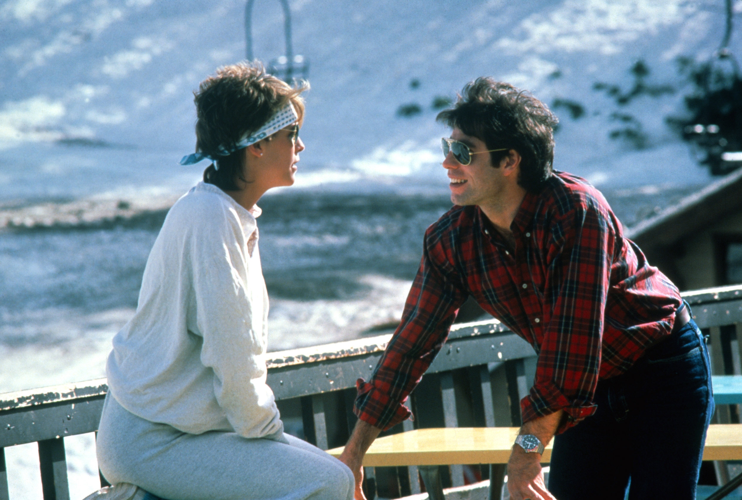 Two people in casual winter attire conversing outside, with snow in the background