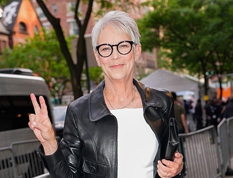 Person in a white dress and black leather jacket offers a peace sign while walking outdoors