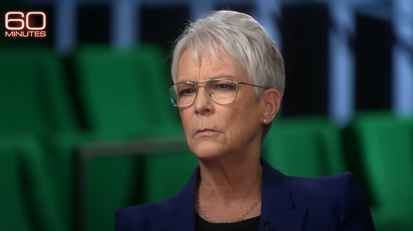 A person with short hair and glasses is interviewed on "60 Minutes," wearing a tailored blazer