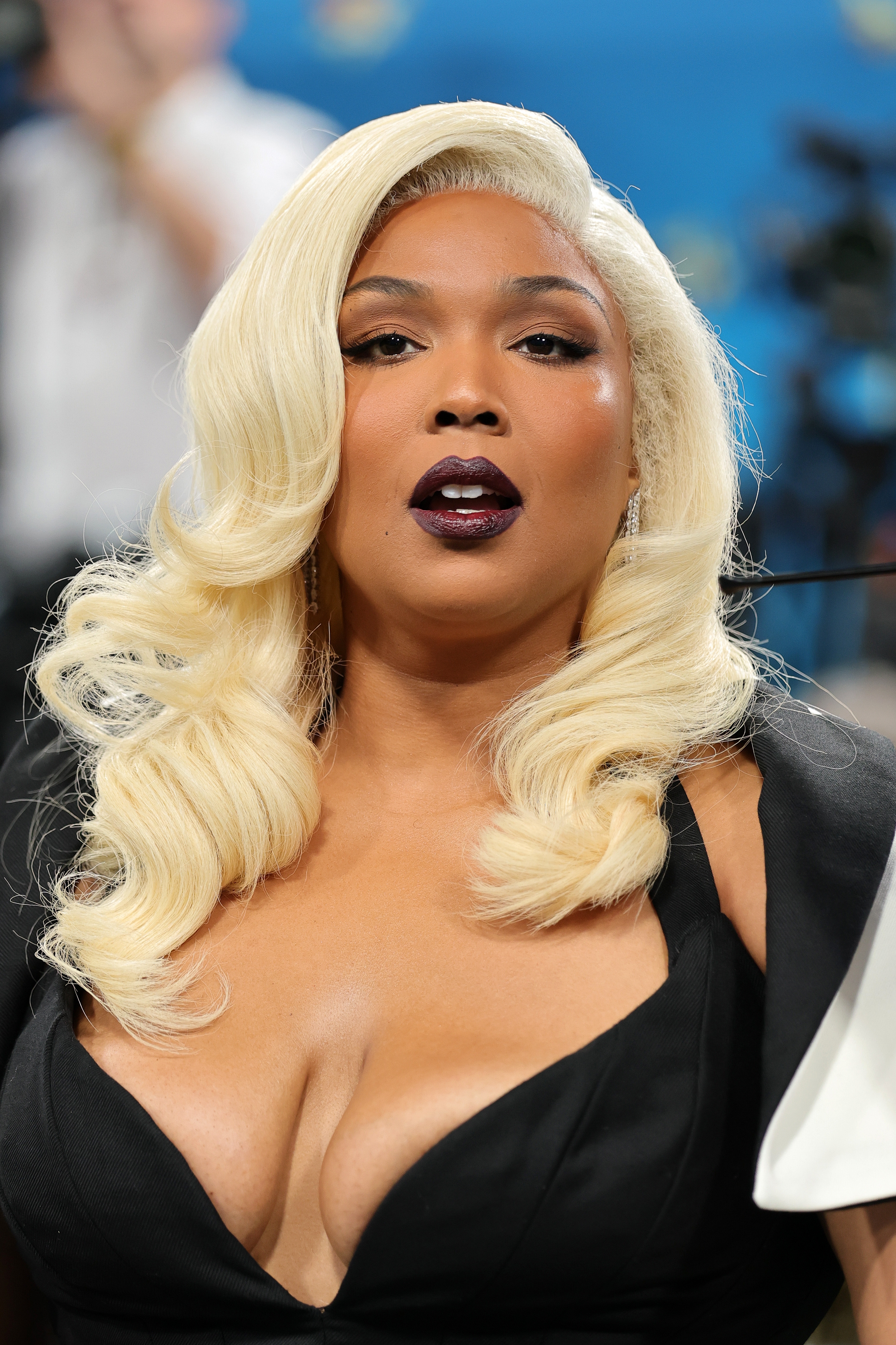 Lizzo with styled blonde hair and bold makeup in an elegant black dress at a public event