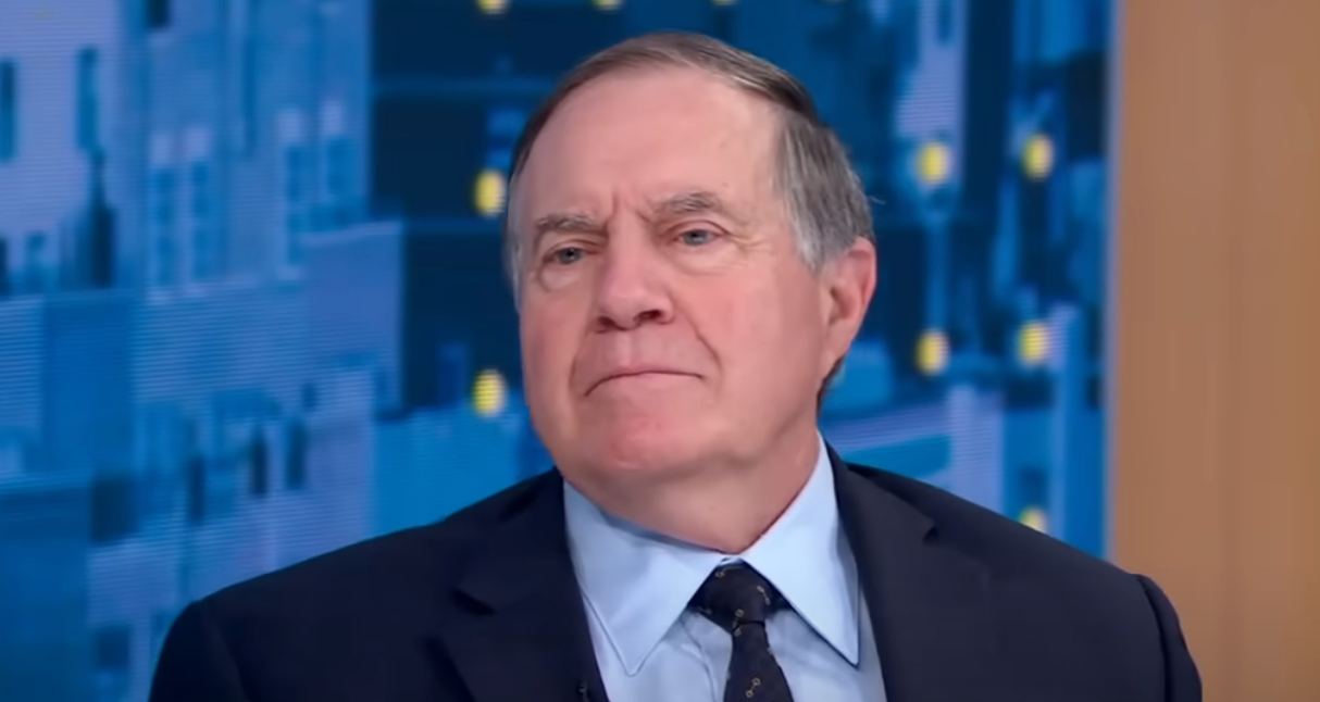 A man in a suit and tie is sitting in a studio with a patterned backdrop