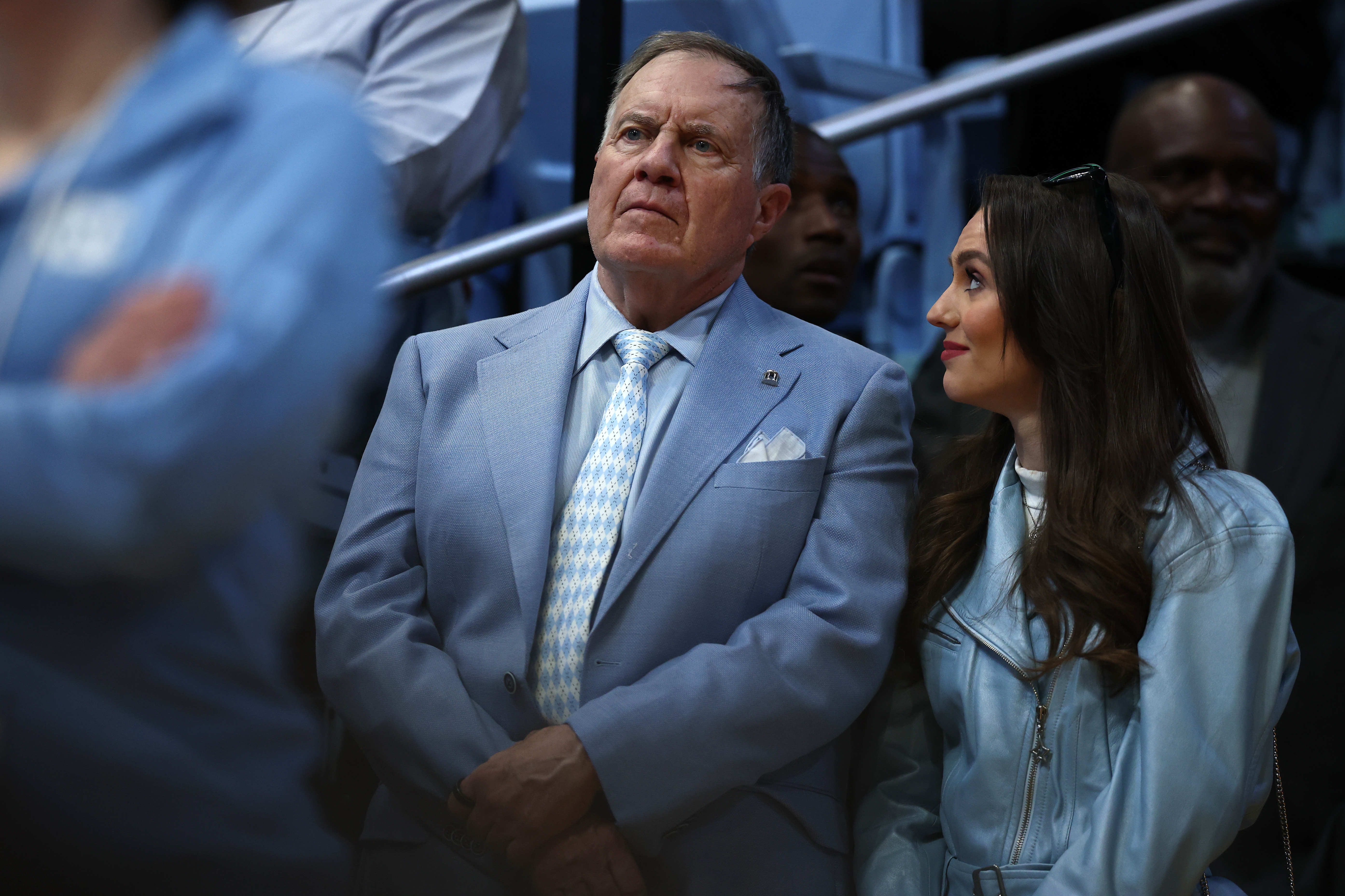 An unidentified man in a light suit and tie stands beside a woman in a light jacket at an indoor event
