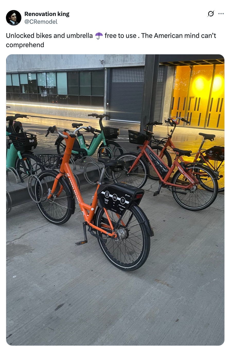Multiple bicycles parked on a sidewalk; one bike has an umbrella mounted. A tweet comments on unlocked bikes being unusual
