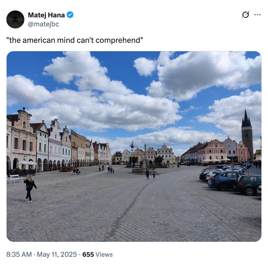 Town square with historic buildings, cobblestone plaza, parked cars, and a church steeple. Tweet text: "the american mind can't comprehend"
