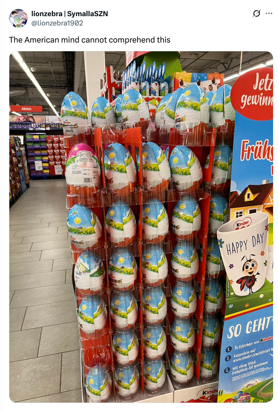 Display of large Kinder Eggs in a store aisle, with a poster that reads "Jetzt gewinnen" and features spring-themed illustrations