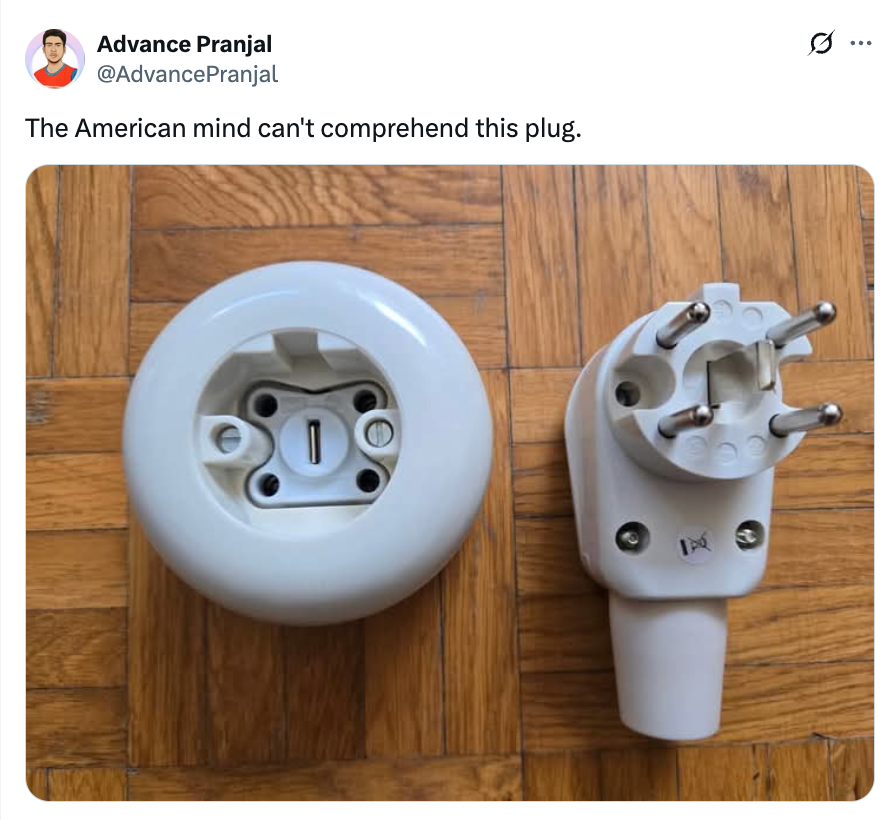 Round power socket and unique plug design with protruding prongs shown on wooden floor; tweet says, "The American mind can't comprehend this plug."