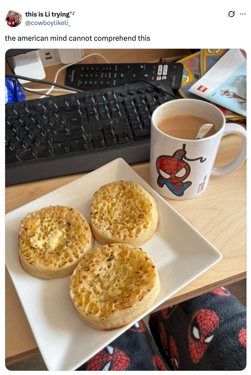 Plate with three crumpets and a mug of tea on a desk, featuring a person wearing Spider-Man pajama pants. Tweet comments on cultural differences